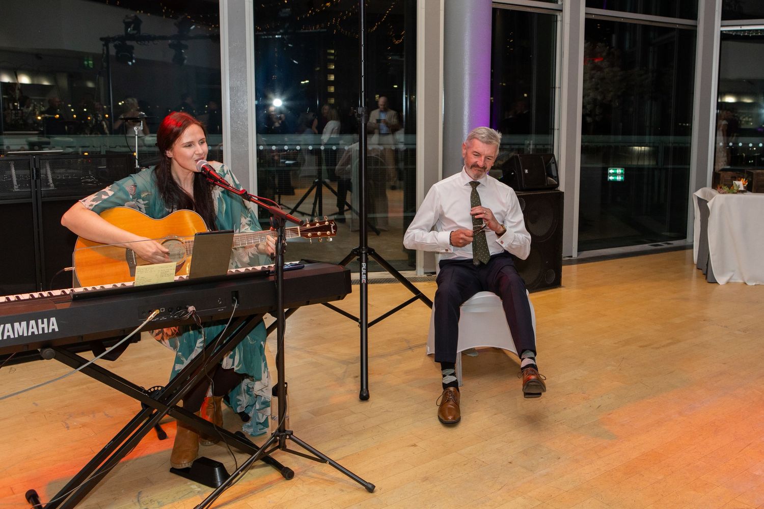 Musicians perform on stage with acoustic guitars and microphones during an intimate indoor concert setting.
