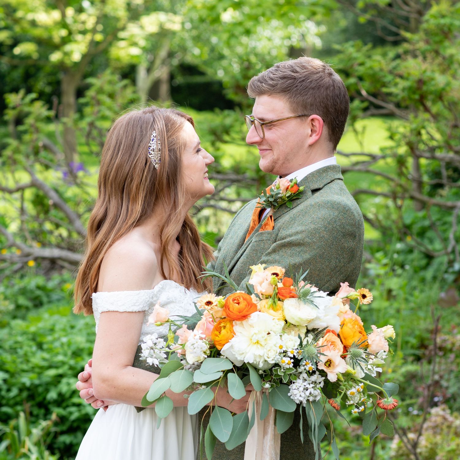 Couple embraces in garden setting with vibrant orange and white wedding bouquet.
