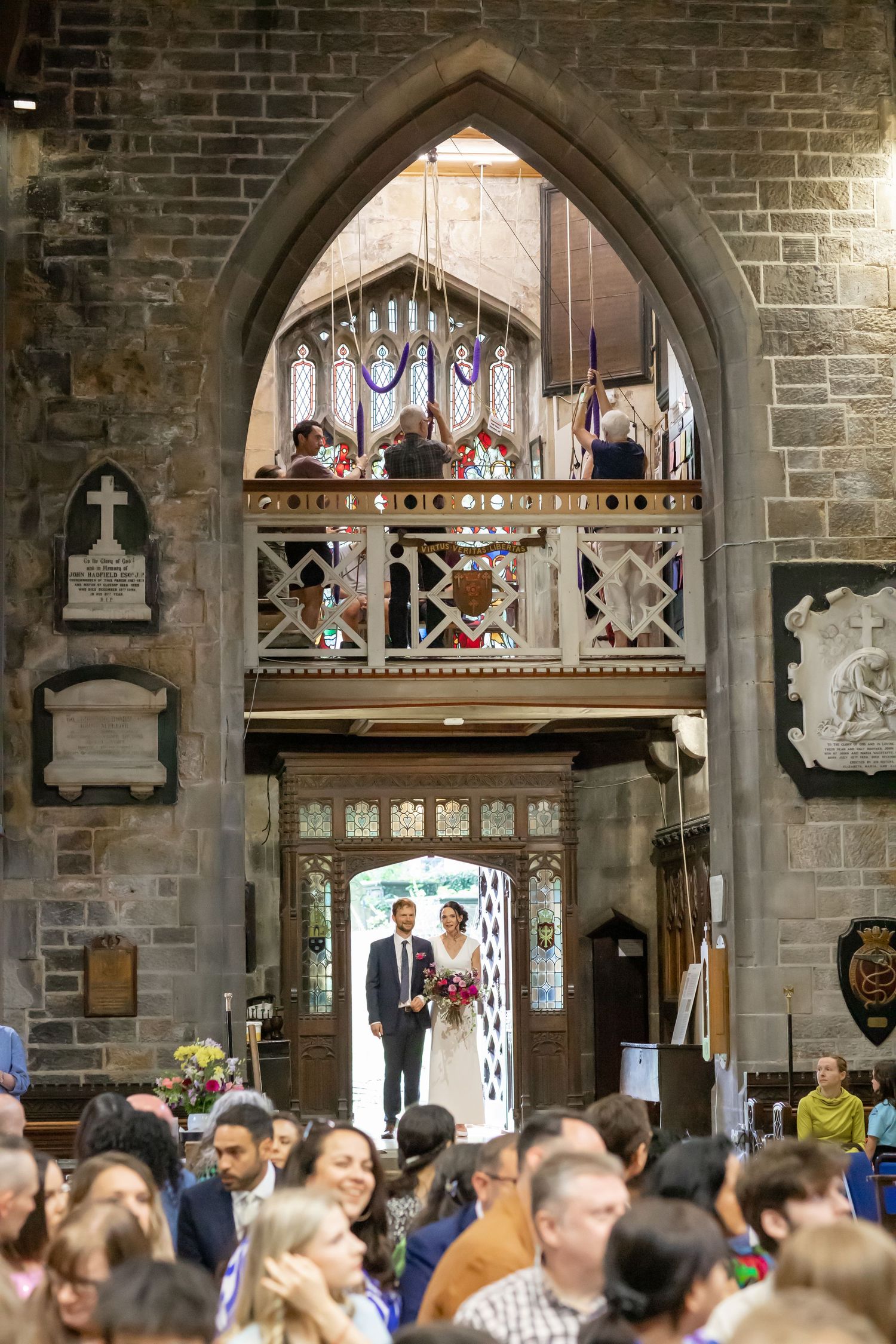 Crowded historic hall with gothic stone archways and people gathering beneath ornate balconies.