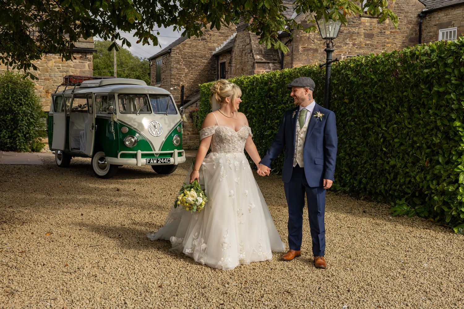 Bride and groom holding hands beside a vintage green VW camper van at a rustic barn wedding venue.