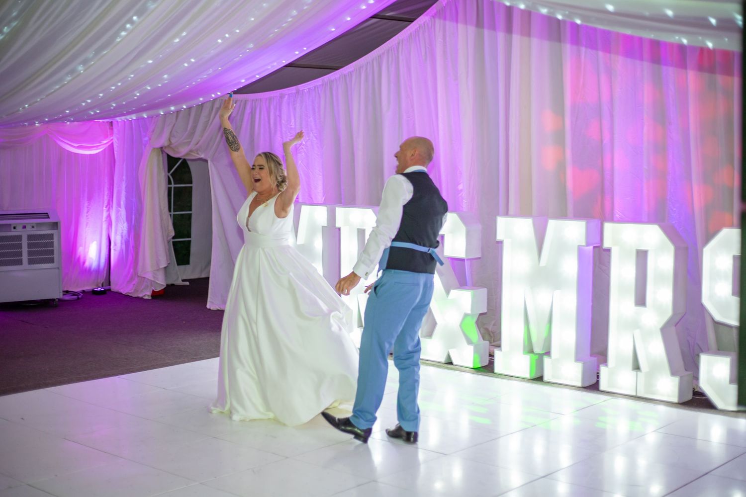 Wedding reception space decorated with purple lighting and glowing MR & MRS letters on display.