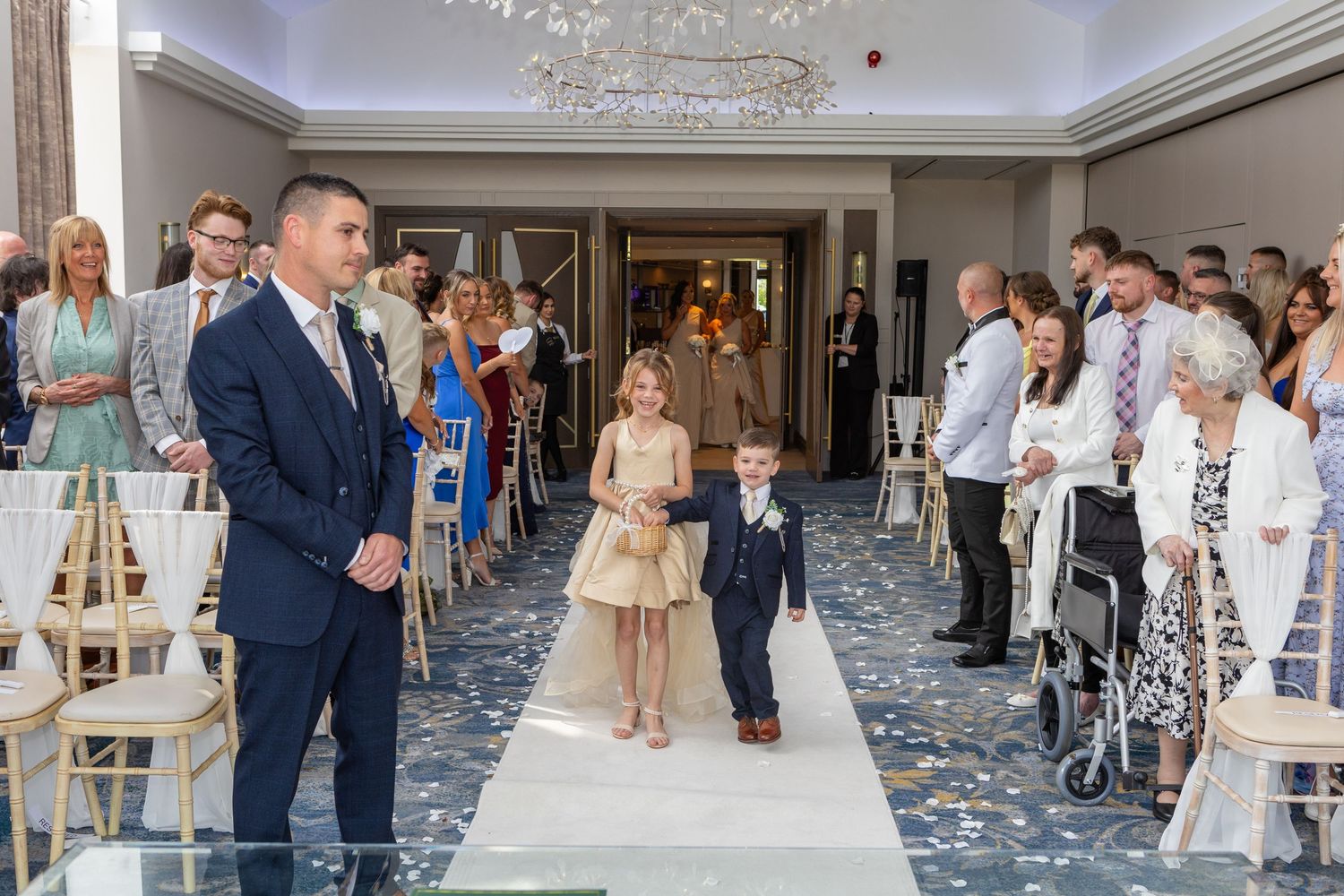 Wedding ceremony processional with attendees lining both sides of an elegant aisle decorated with white lanterns.