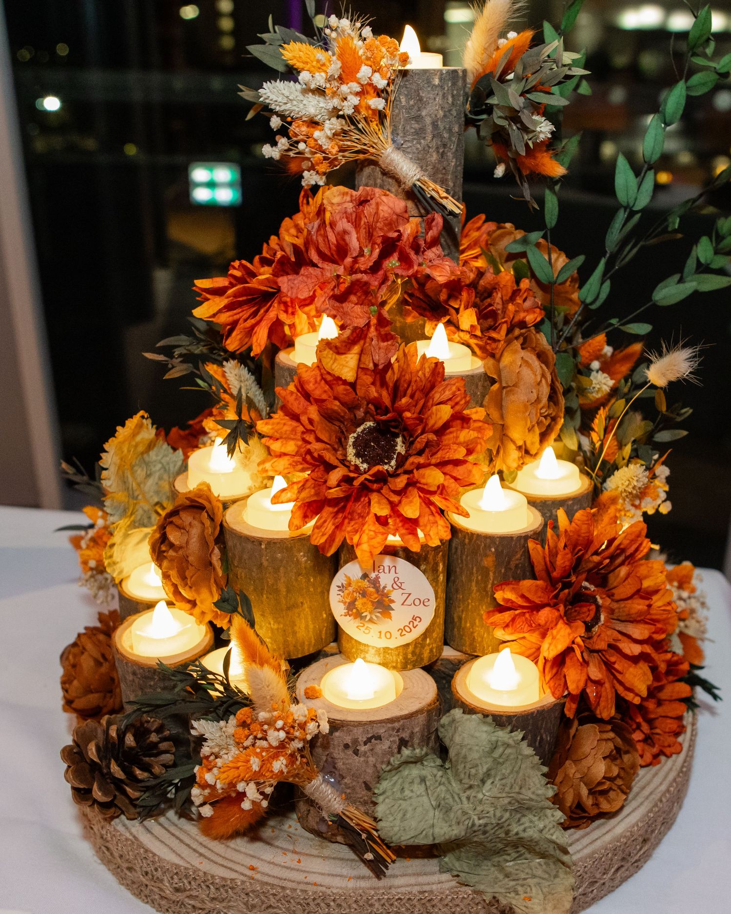 Rustic fall centerpiece with orange dahlias, pinecones, and glowing tea lights arranged on wooden log slices.