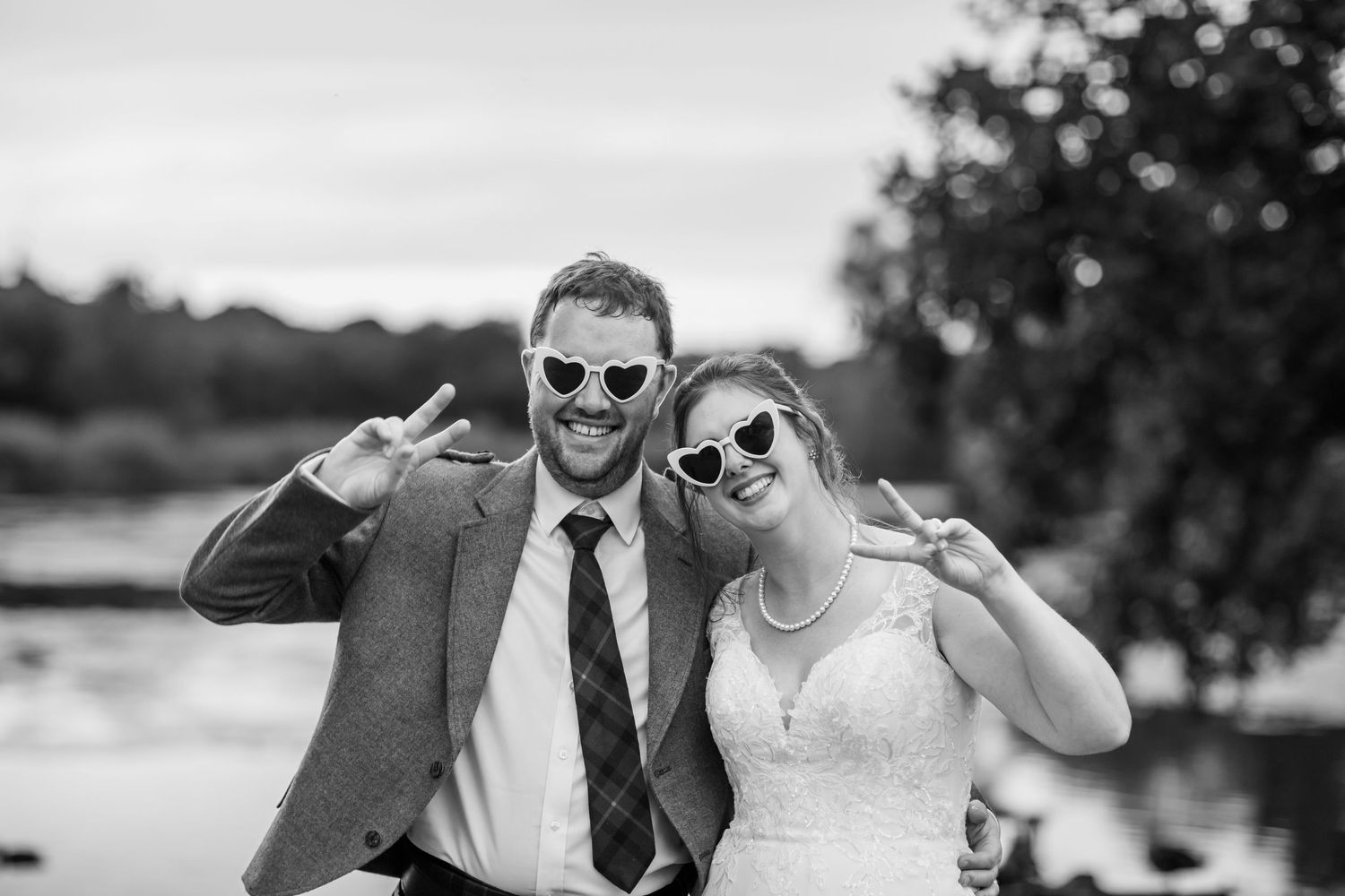 Fun wedding portraits with sunglasses and poses against a sunset lake backdrop.