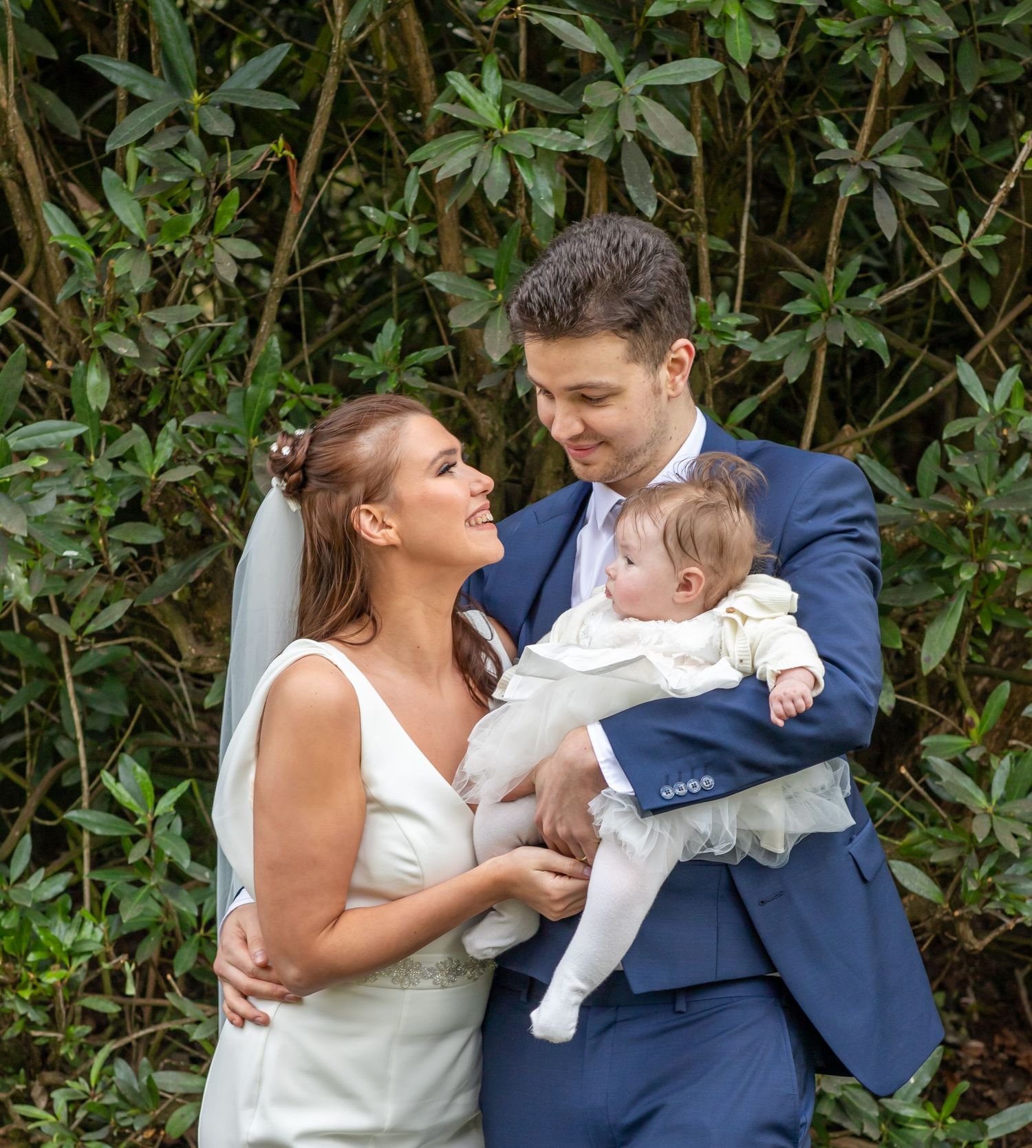 A joyful family moment with a baby against a backdrop of green foliage.