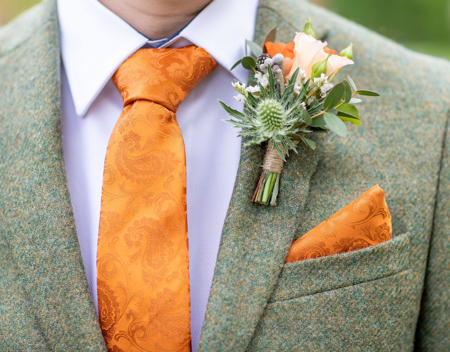 Close-up of orange tie and boutonniere against green tweed suit jacket.