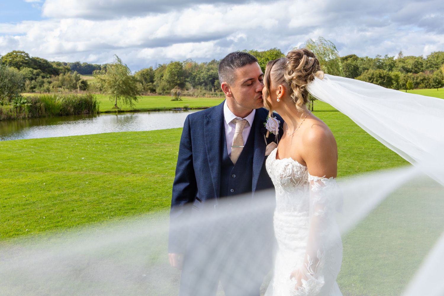 A couple shares a romantic moment together on a scenic golf course with a lake and lush greenery in the background.