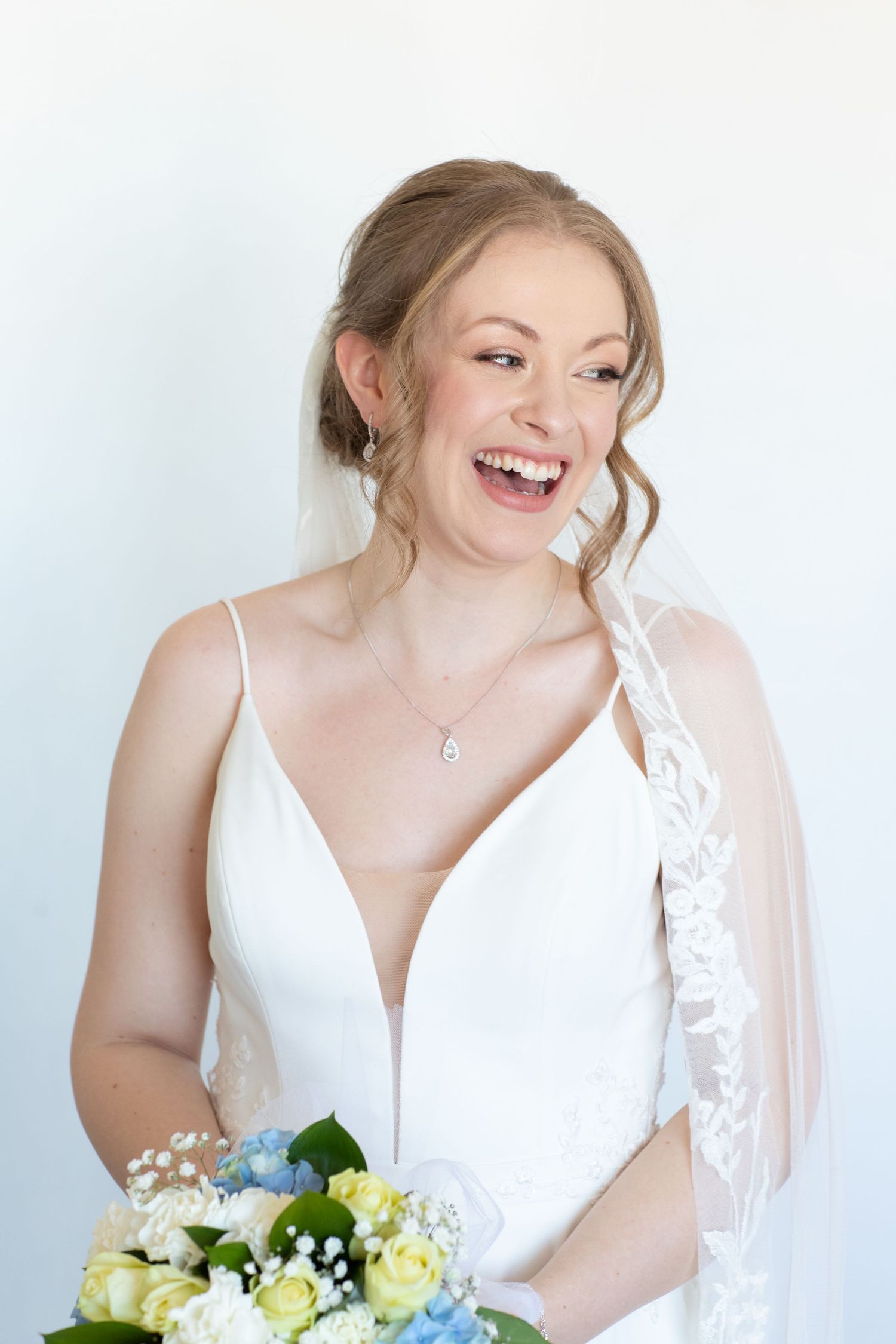 Bride wearing plunging neckline dress holds bouquet while laughing.