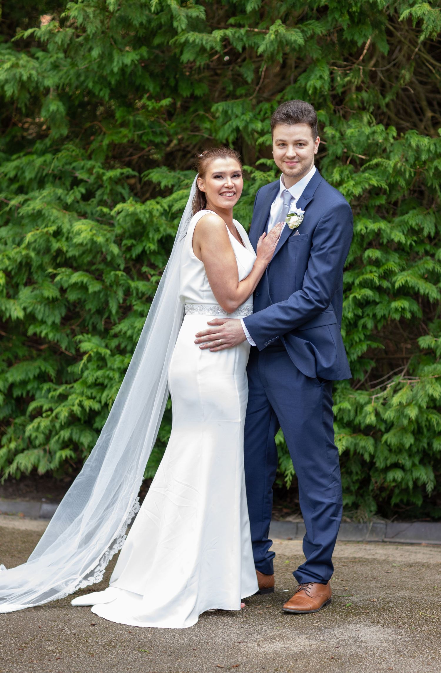 A romantic wedding portrait on a garden path with lush greenery in the background.