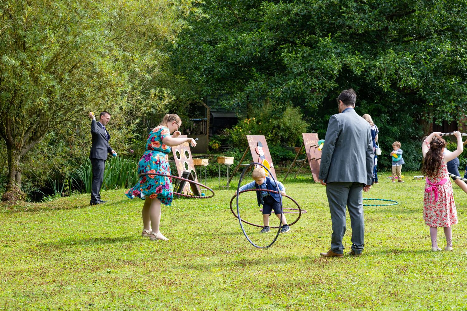 Children and adults gather in a grassy park area for outdoor recreational activities on a sunny day.