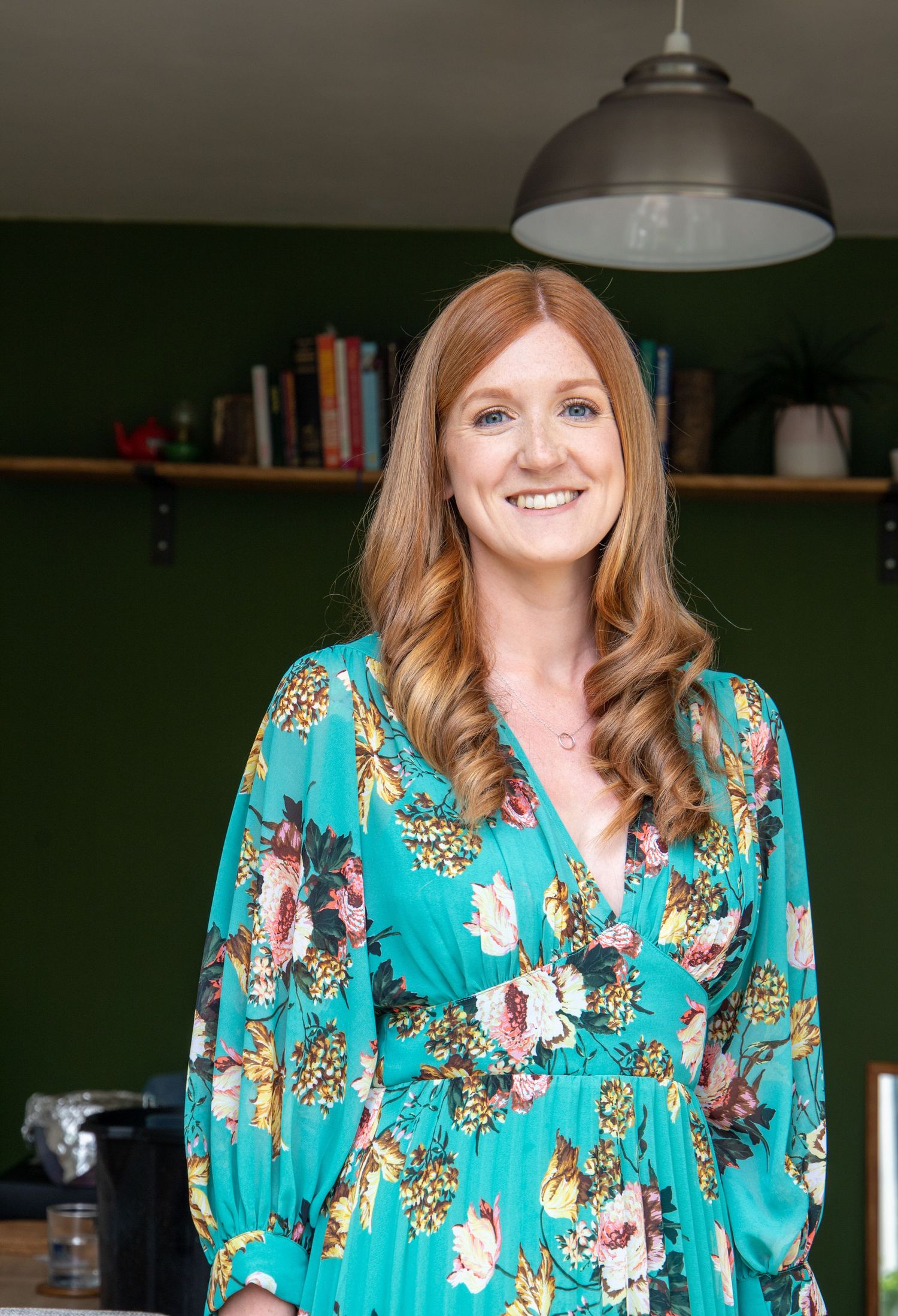 Person wearing turquoise floral dress smiling in casual indoor setting.