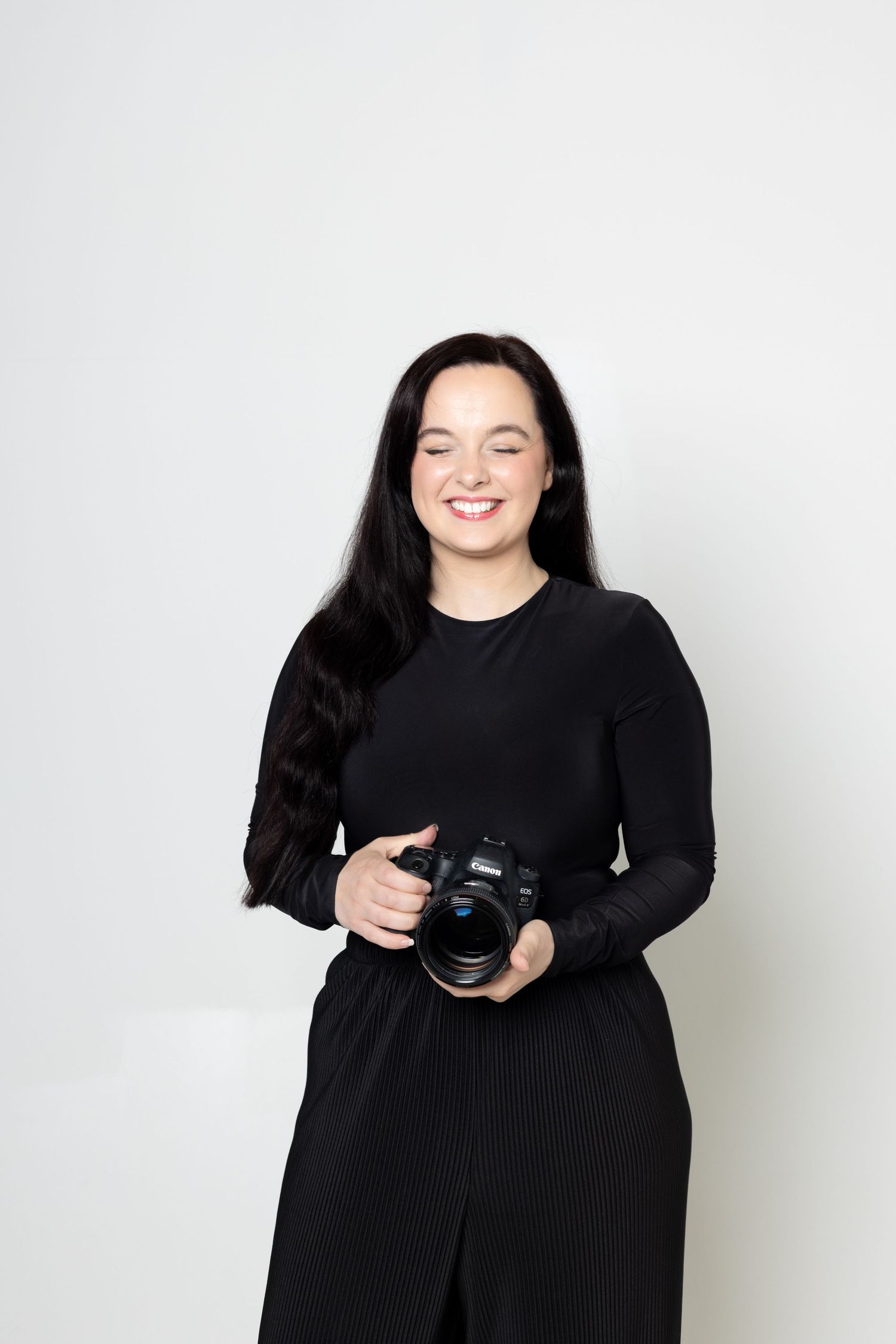 Professional photographer smiling while holding DSLR camera against white background.