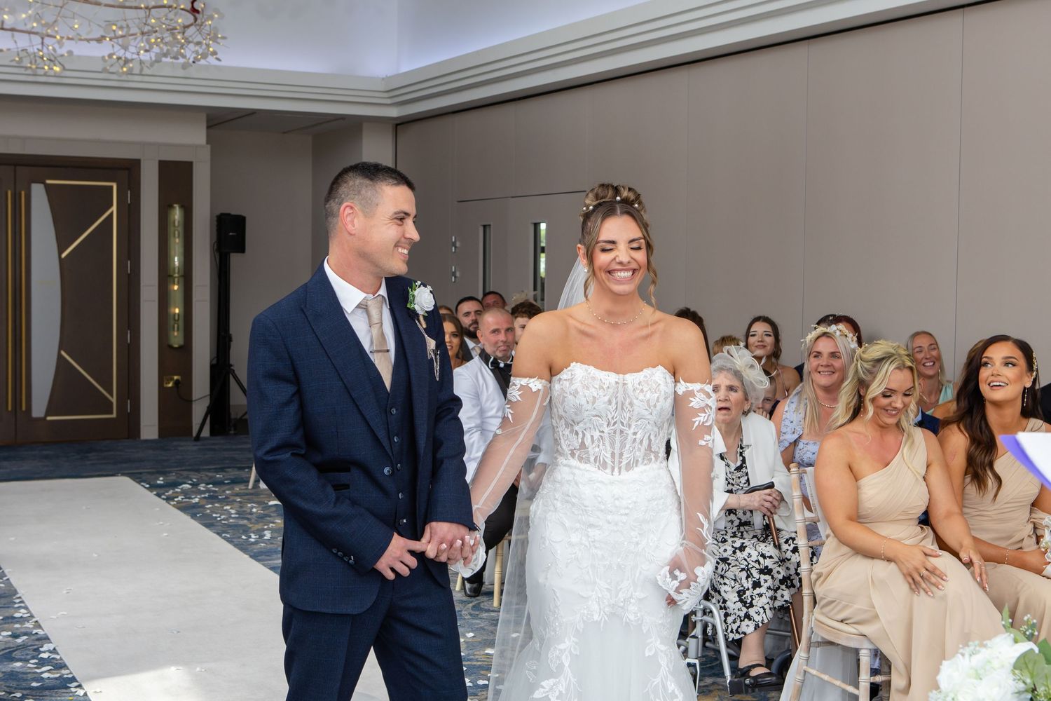Wedding couple shares their first dance surrounded by guests at an elegant indoor reception venue.
