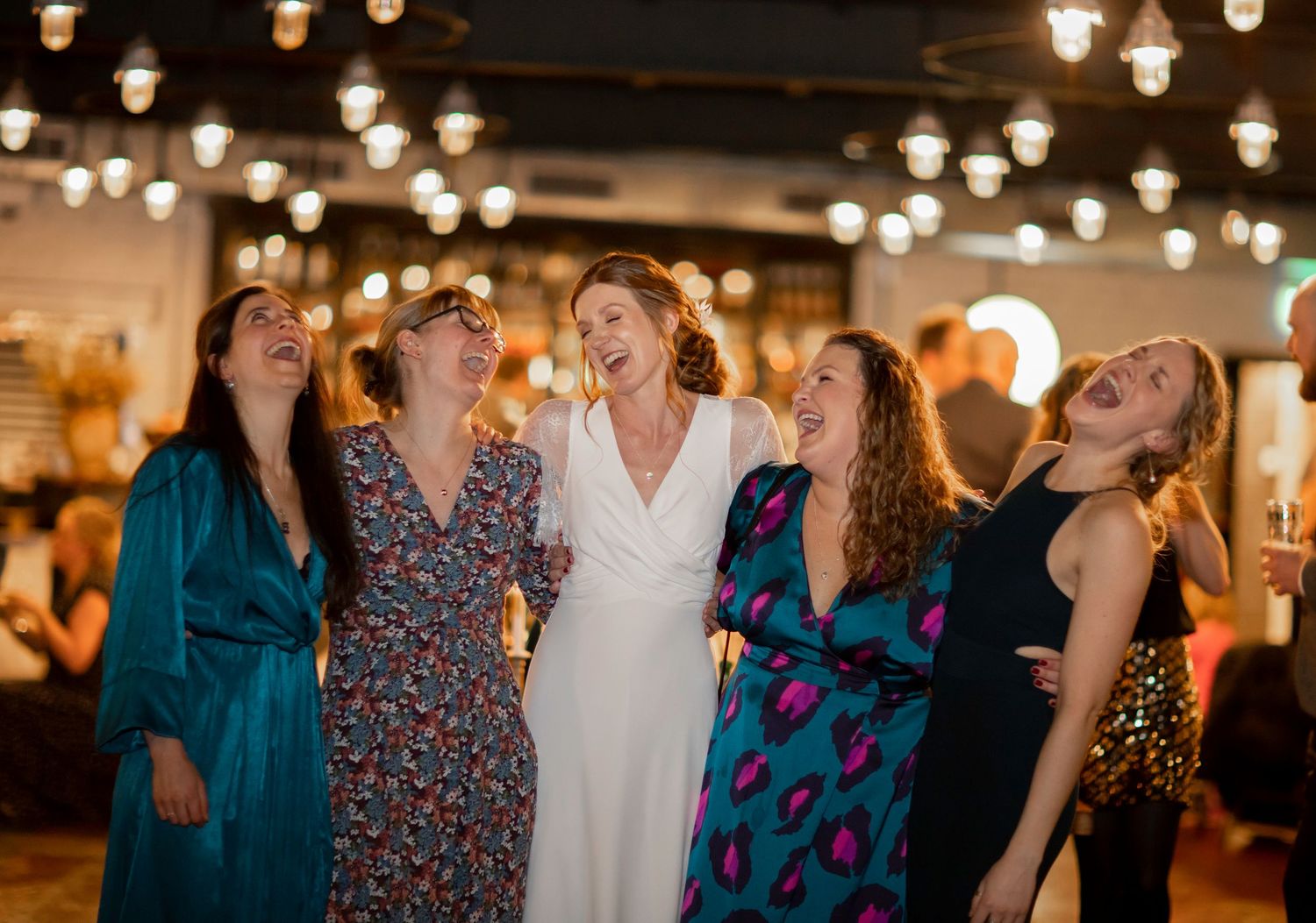Wedding party dancing and celebrating under atmospheric pendant lighting.