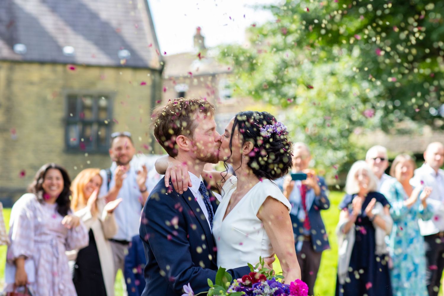 Wedding guests celebrating outdoors with confetti in a garden setting.