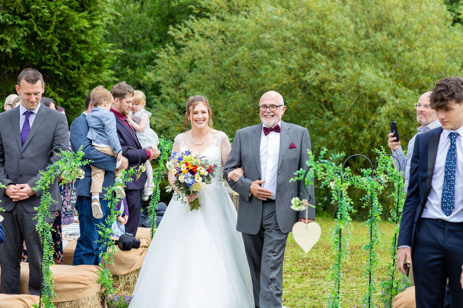 Wedding party and guests gather outdoors in a lush garden setting during a summer celebration.