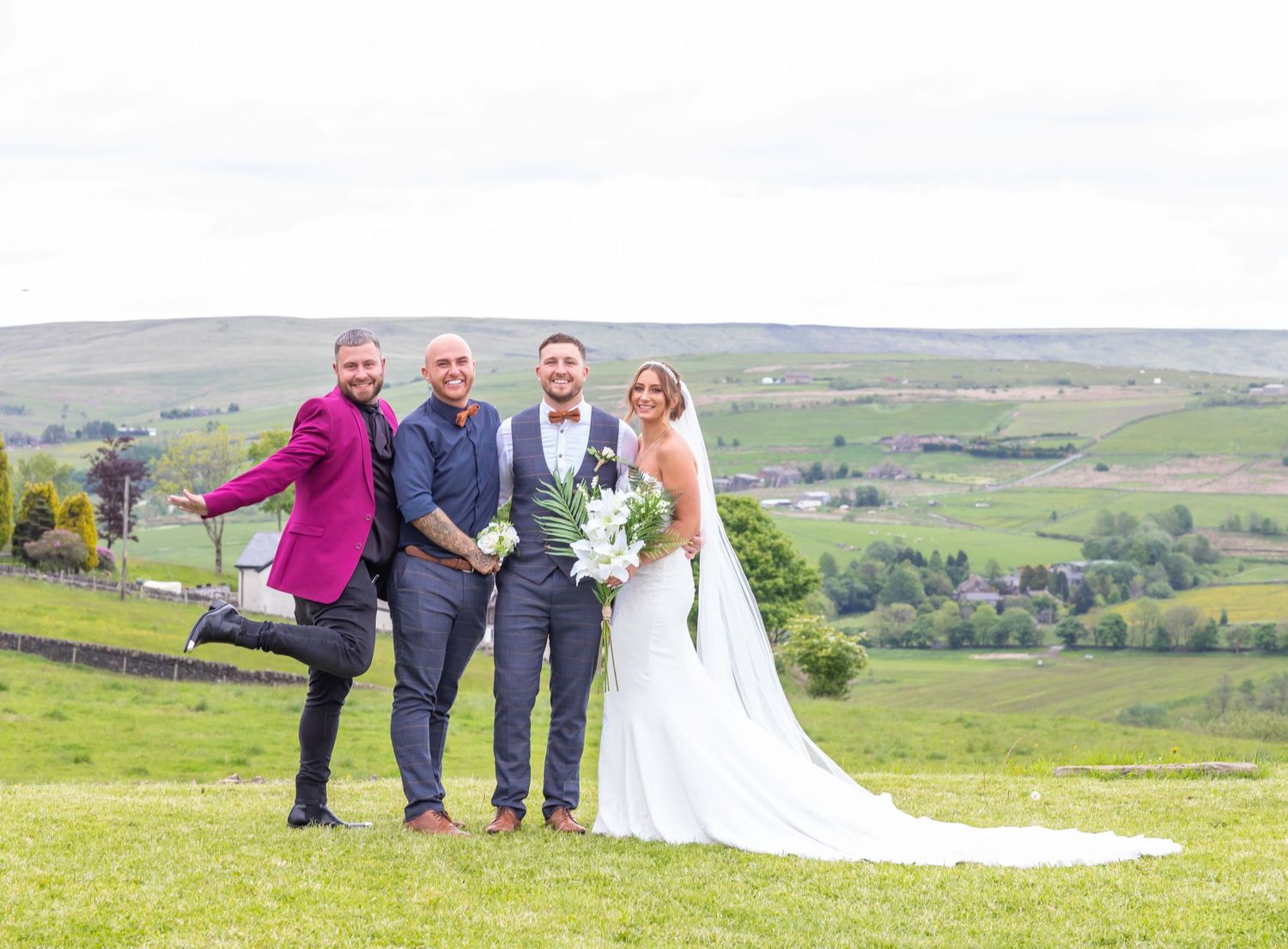 Wedding party having fun posing for photos on a scenic hilltop overlooking green rolling countryside.