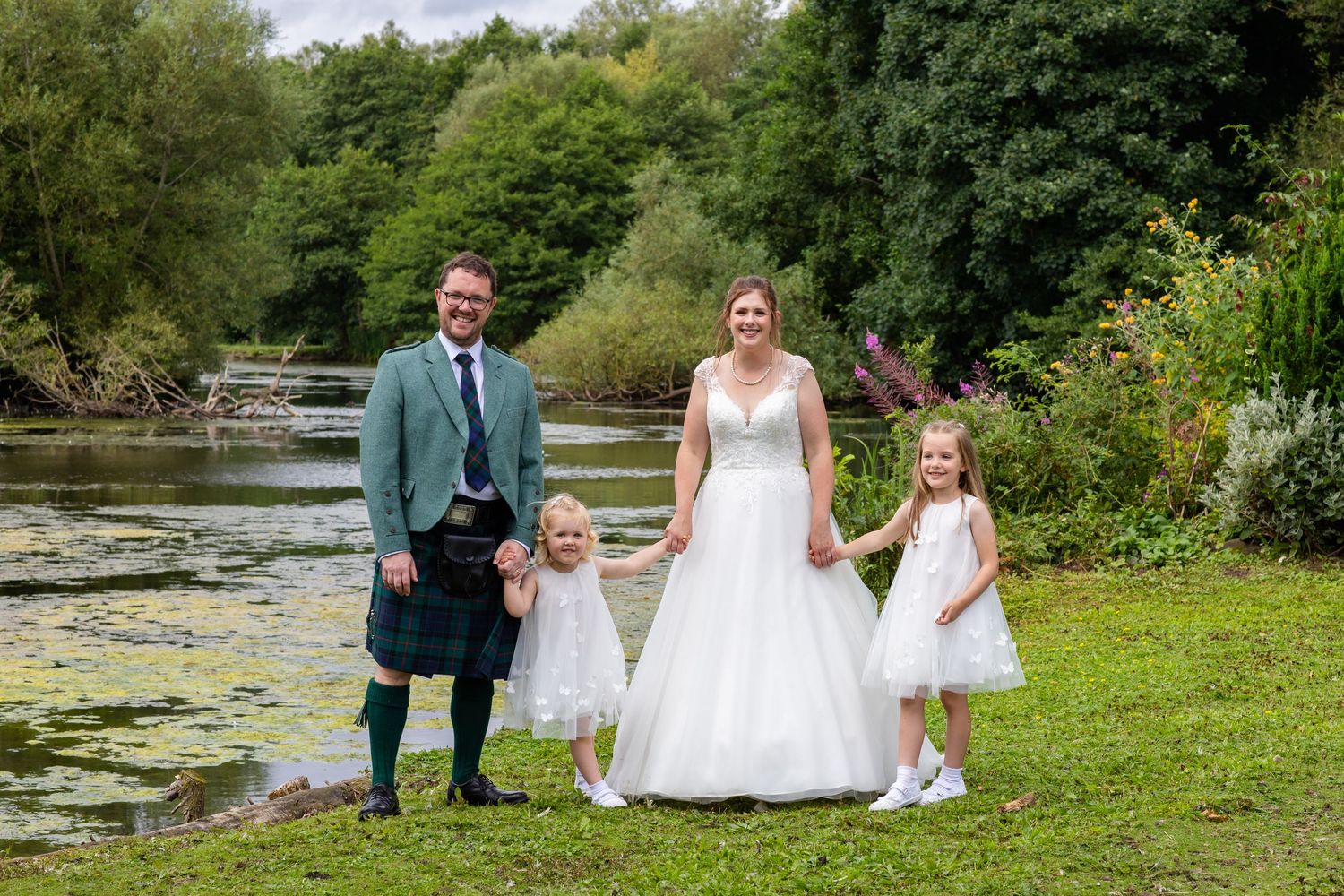 Wedding party poses for photos in a scenic garden setting with natural landscaping and water features.