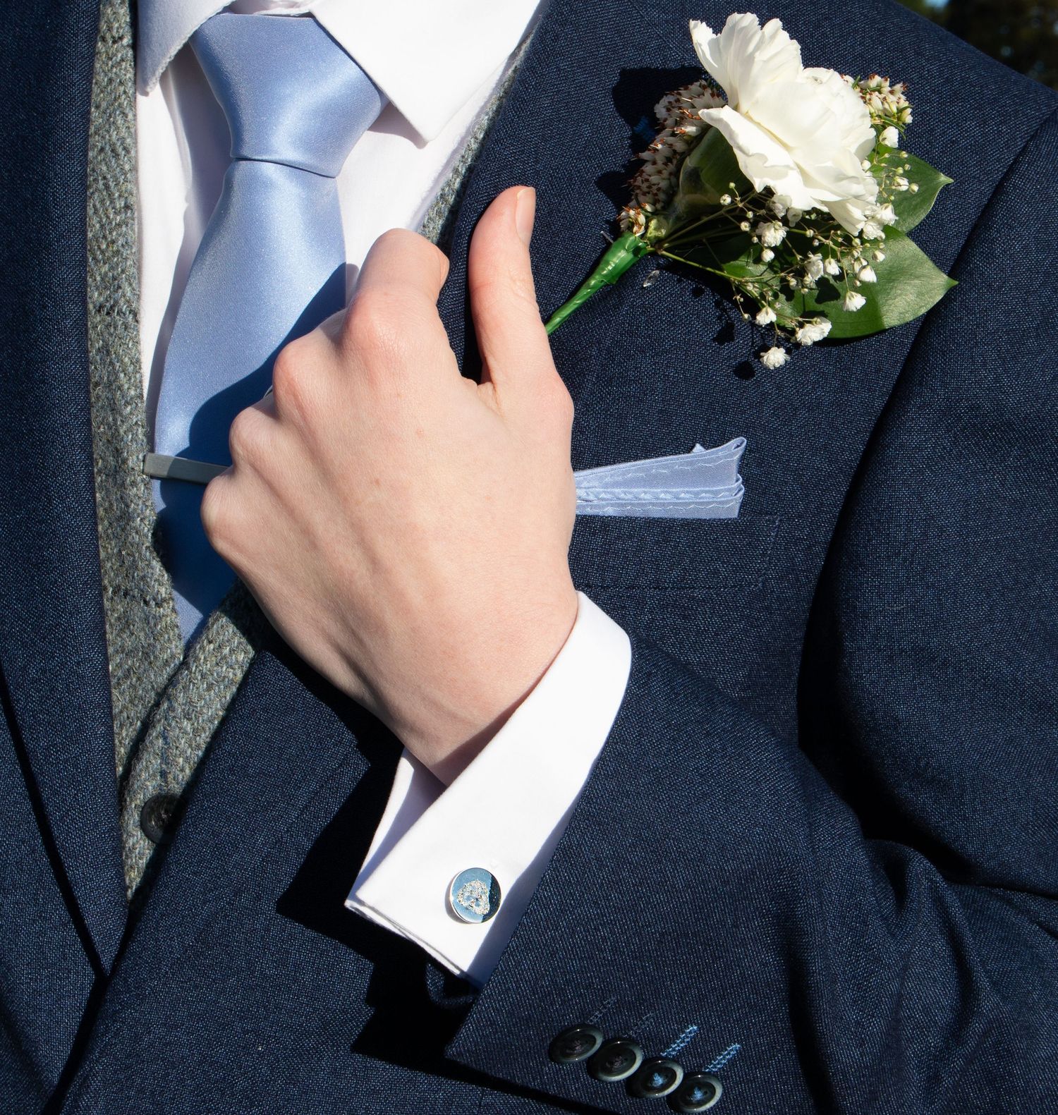 Close-up of a navy suit with light blue tie and white rose boutonniere.