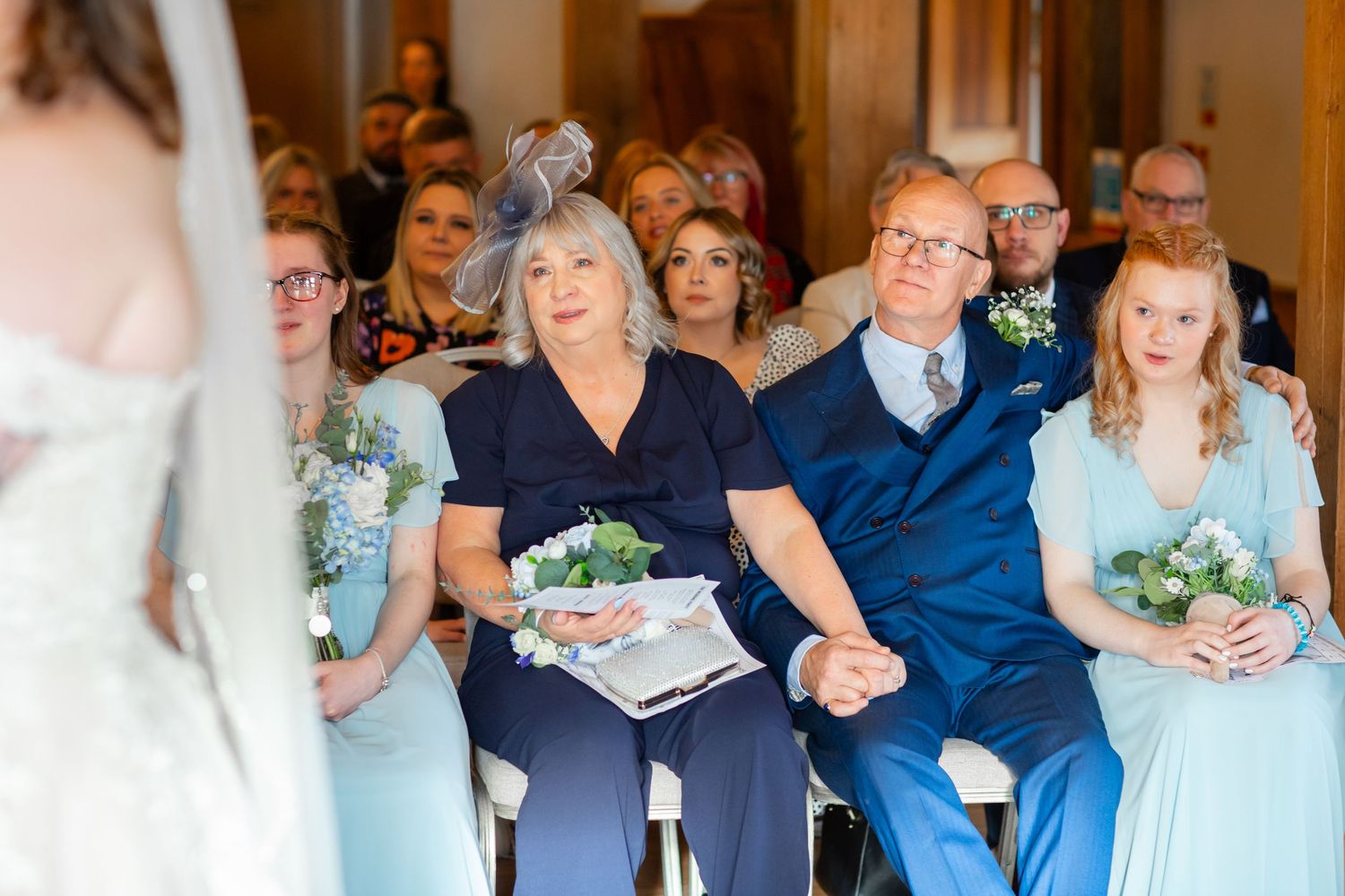Wedding guests share emotional reactions during a ceremony while seated in rows of chairs.