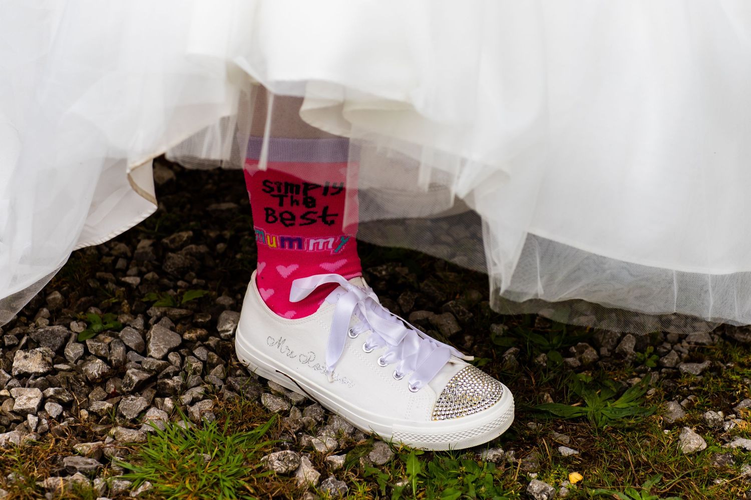 A close-up view of a white sneaker with rhinestone embellishments against a natural outdoor background.