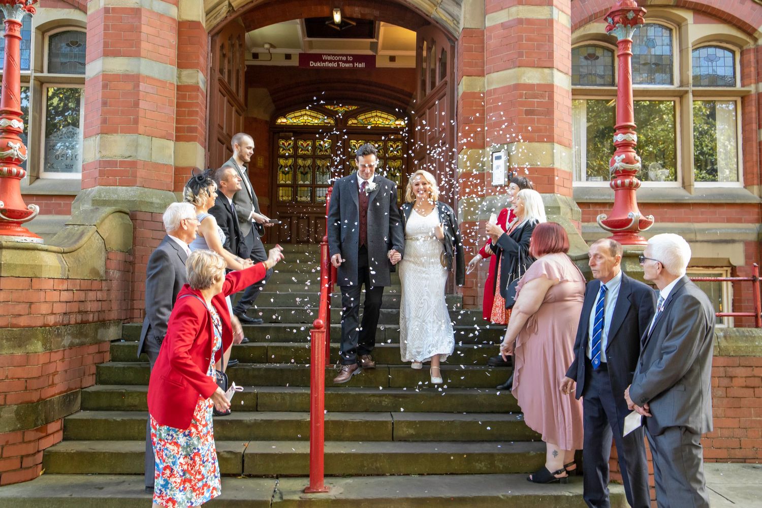 Wedding party and guests gathered outside historic red brick church entrance.