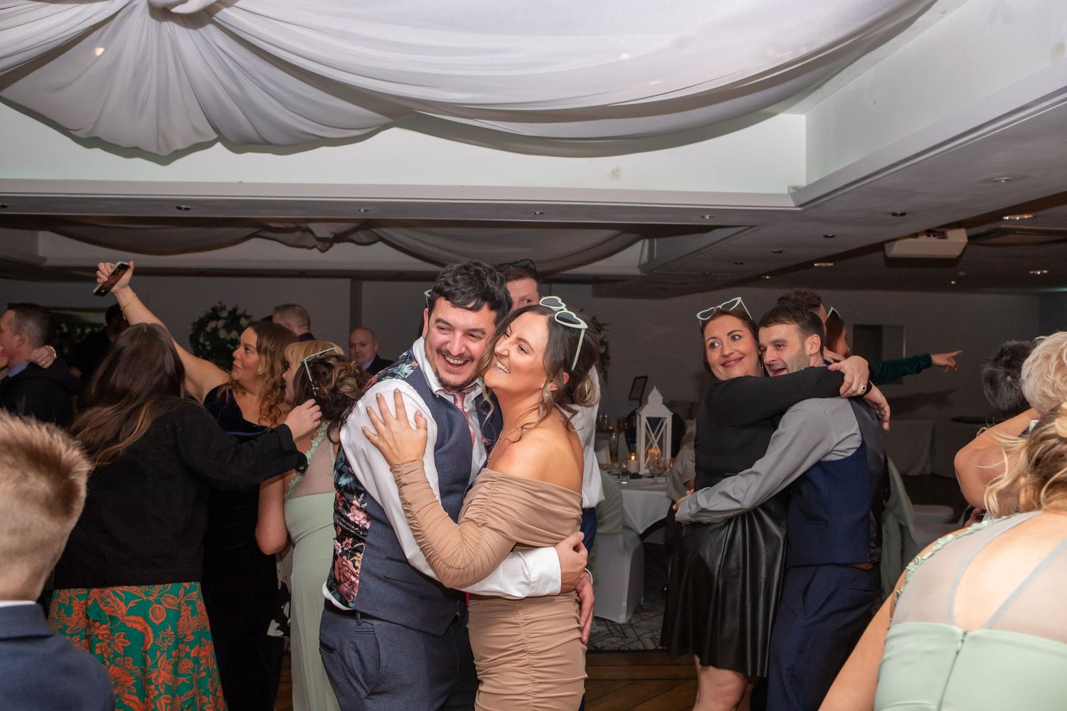 Couples dancing together at a wedding reception under draped white fabric ceiling decorations.