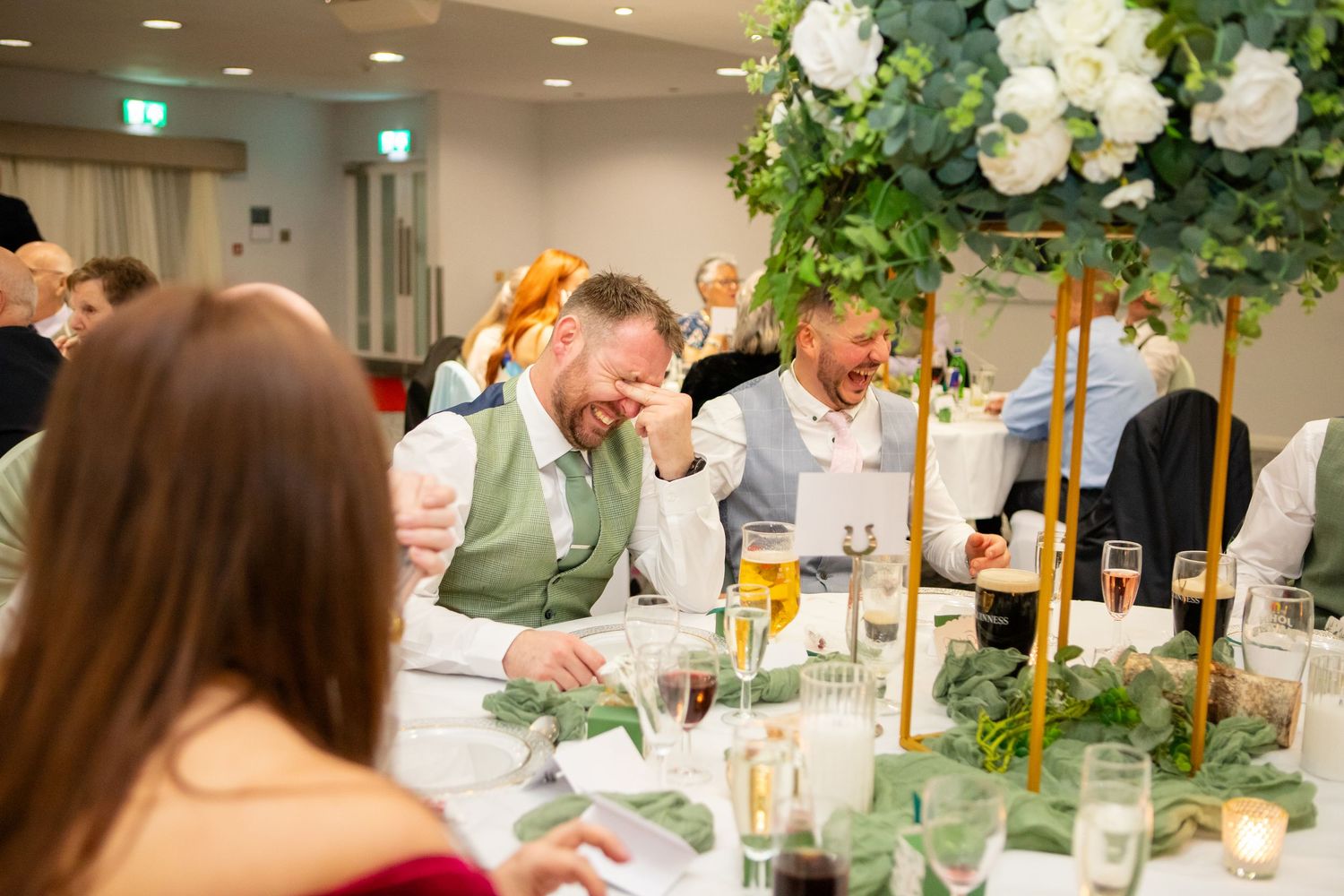 Elegant wedding reception table settings with white floral centerpieces and glowing candles in a modern banquet hall.