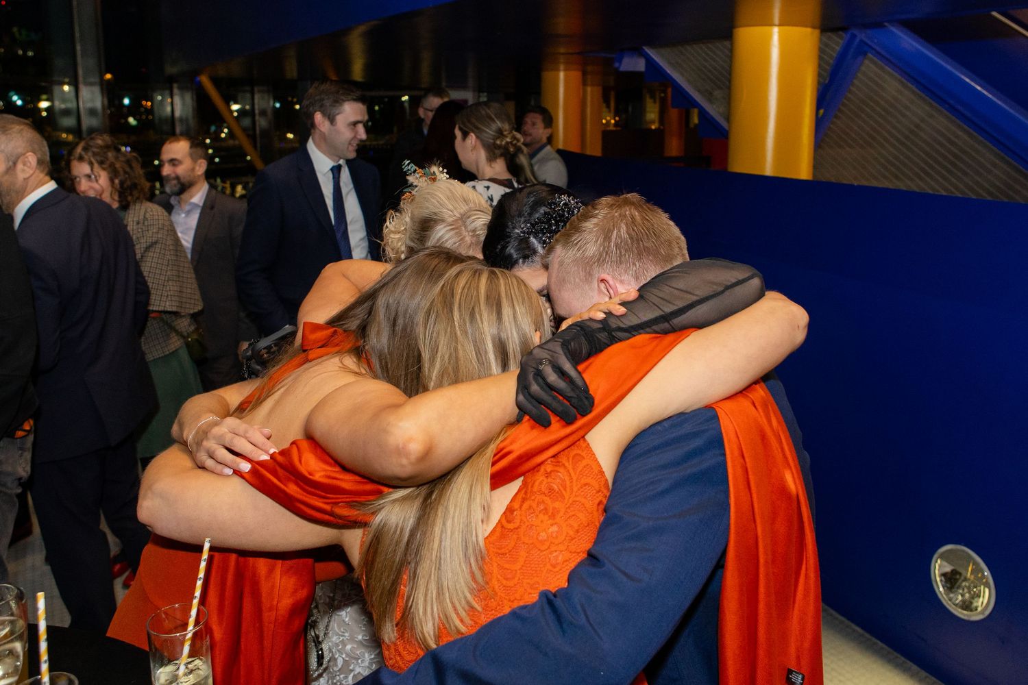 A group of people embrace each other while wearing orange and blue attire at an event.