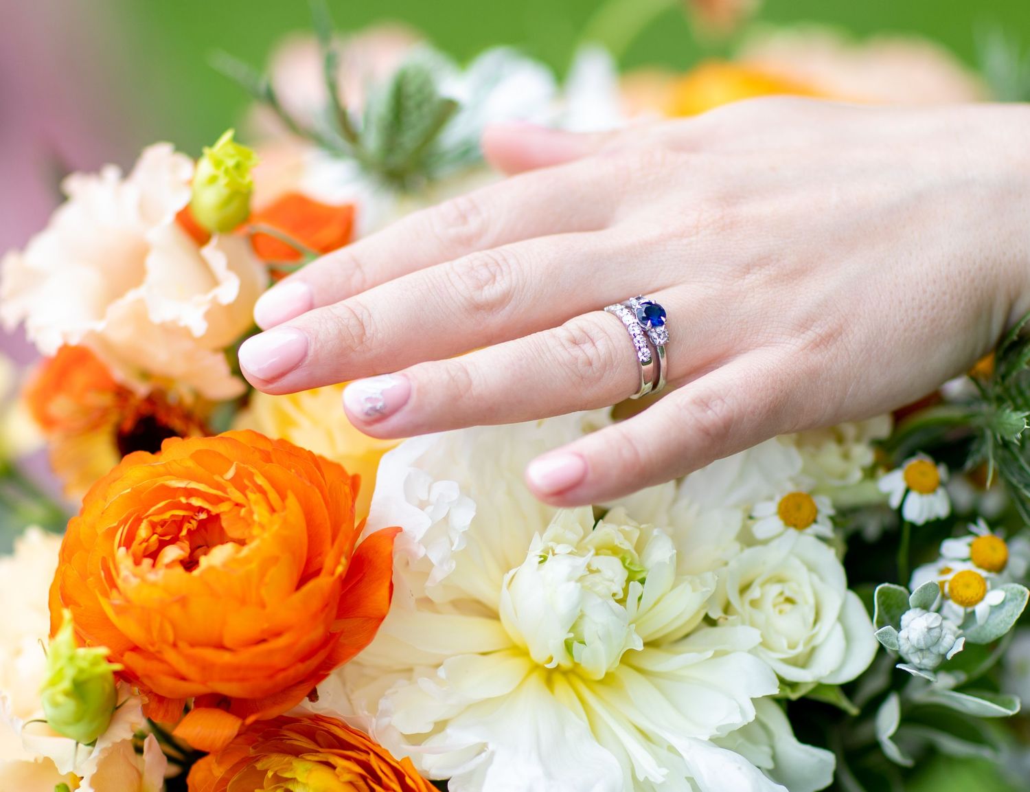 Hands arranging vibrant orange ranunculus and white daisies in a floral bouquet.