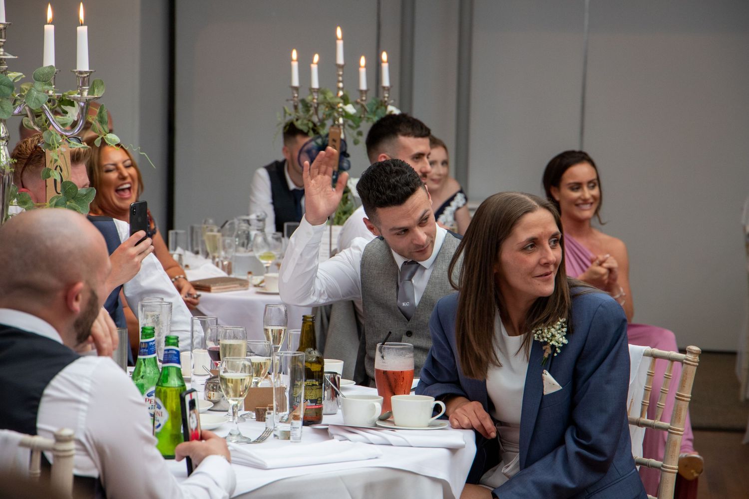 Wedding reception dinner setting with lit candelabras and elegant table settings in an indoor venue.
