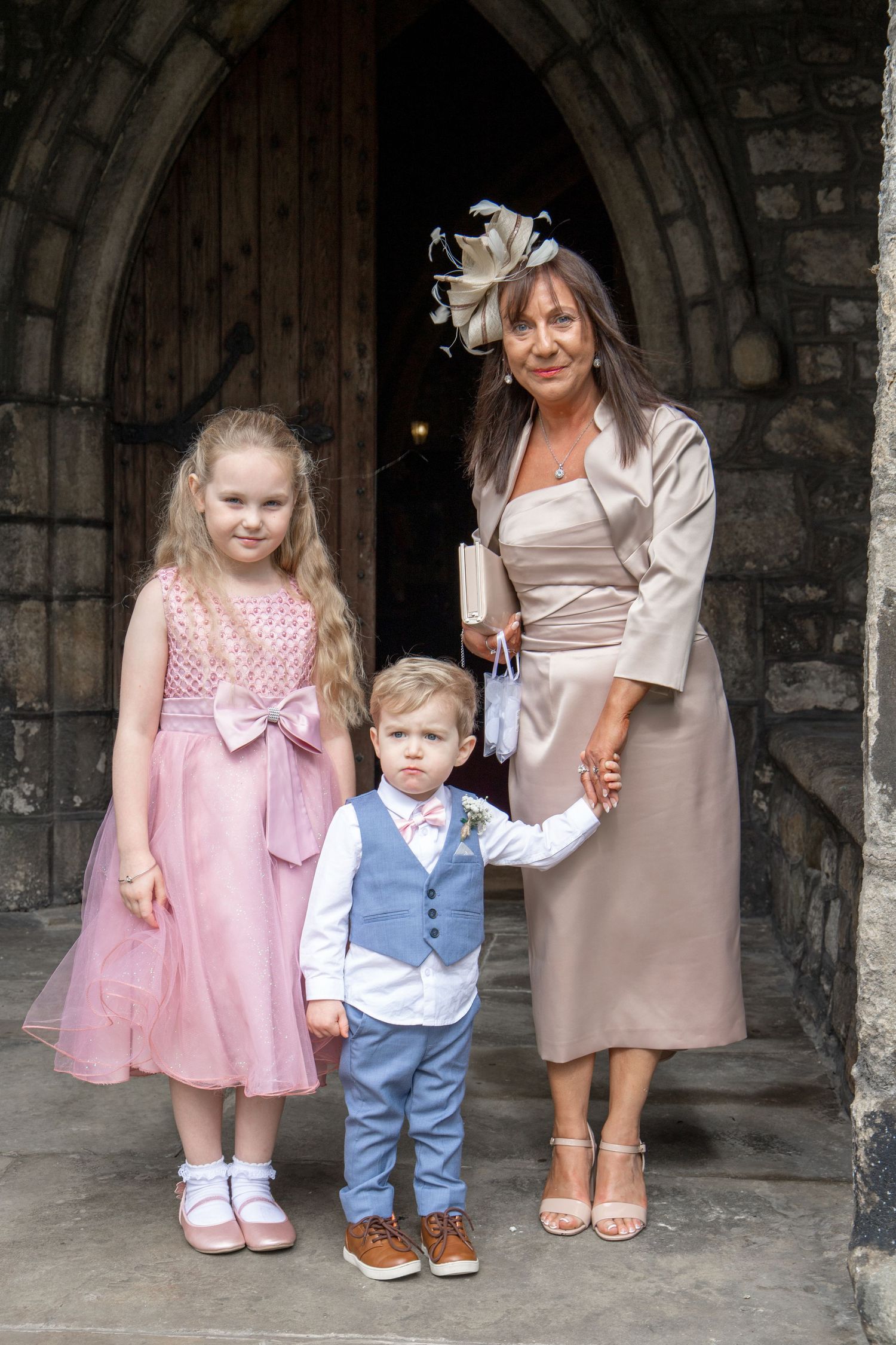 Wedding party members in pink and blue outfits posing under a stone archway.