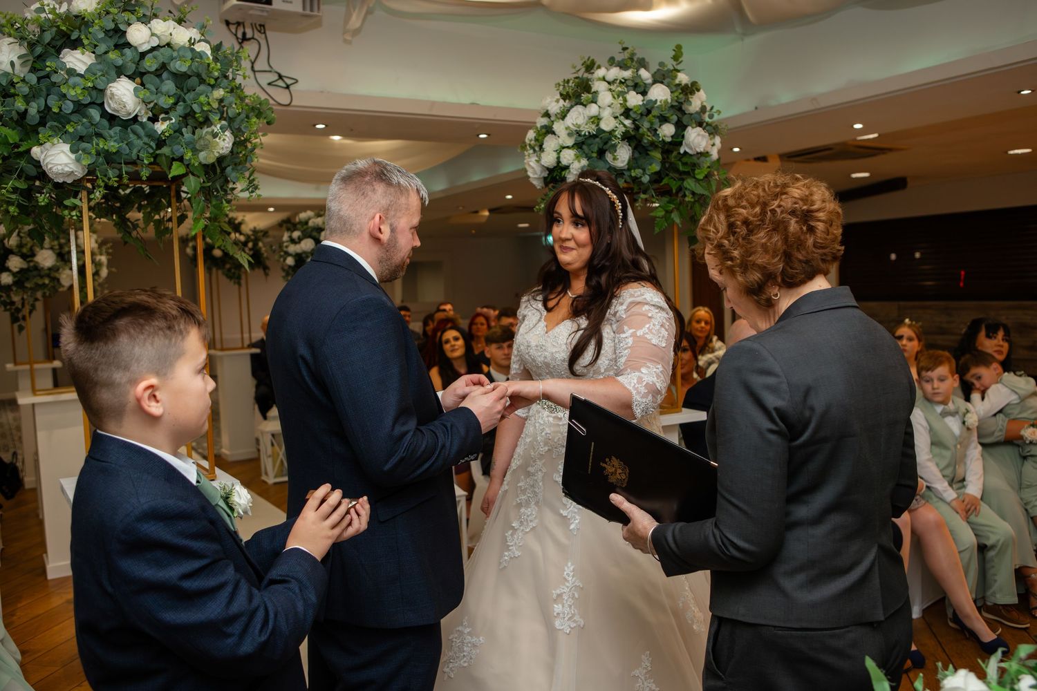 Wedding ceremony in progress with officiant and guests in decorated indoor venue.