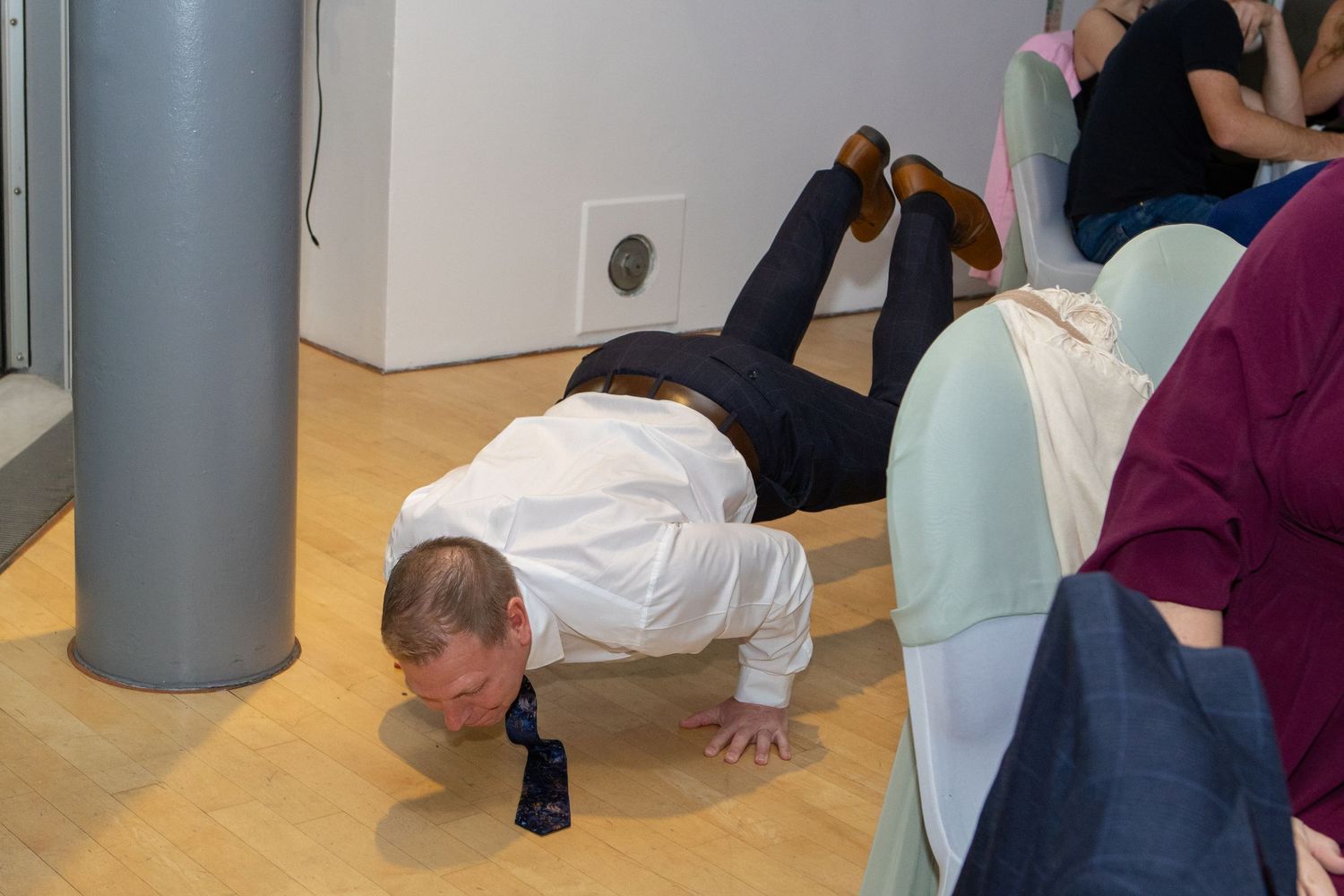 A person in a white shirt performs a push-up exercise on the floor of what appears to be an office or meeting space.