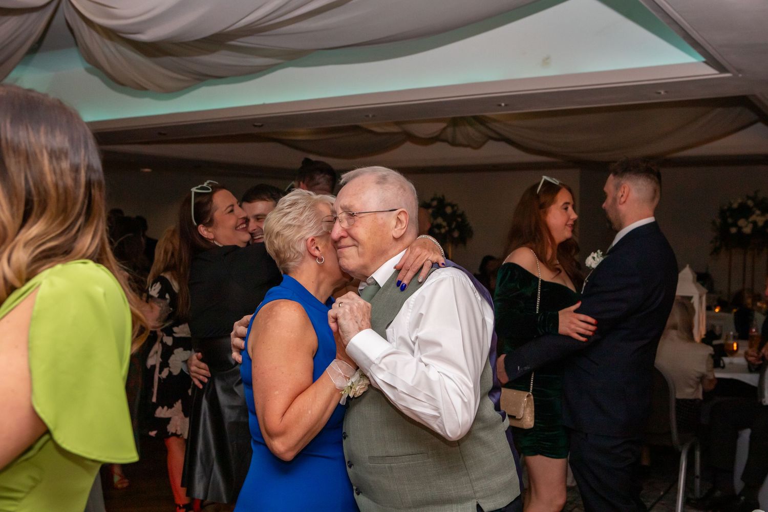 People dancing together at a wedding reception under draped fabric ceiling decorations.