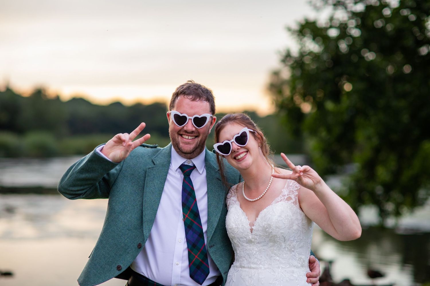 Wedding couple posing playfully for photographs at sunset by a lake.