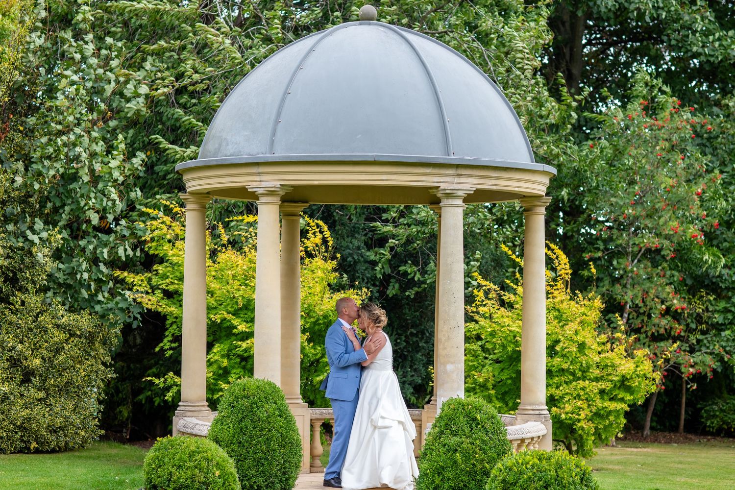 A beautiful white gazebo with domed roof set in a manicured garden creates an elegant backdrop.