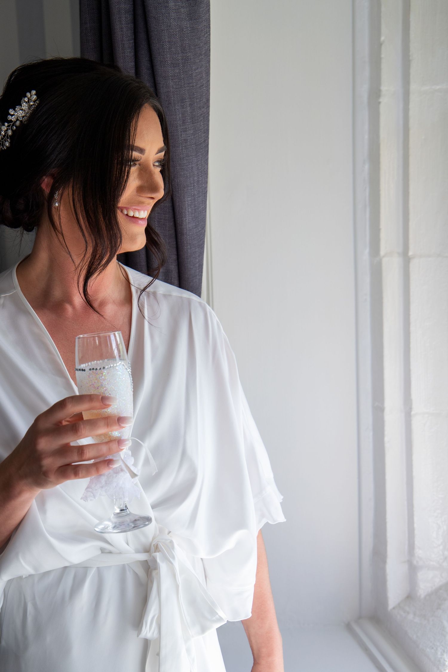 Person in white robe holding champagne glass against white wall backdrop.