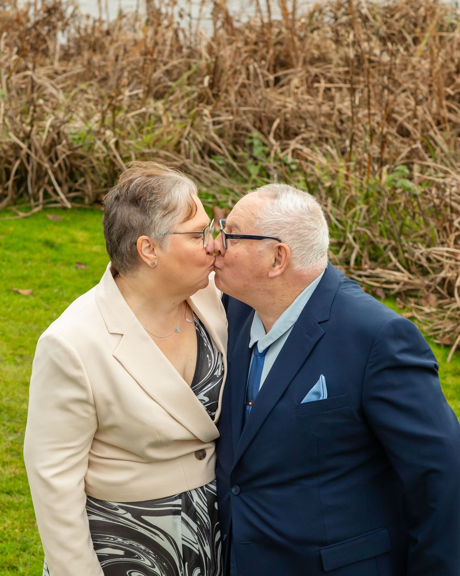 A couple shares an intimate moment outdoors against a natural backdrop of dried foliage.