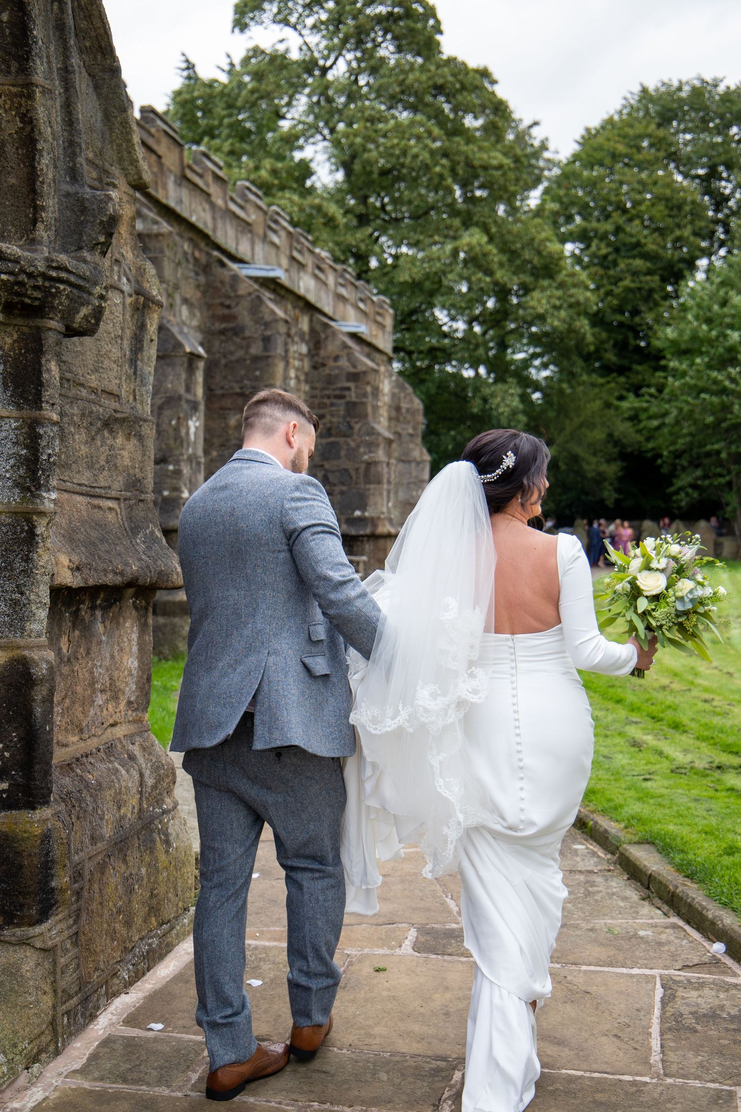 A couple in wedding attire walking along a historic stone wall pathway.