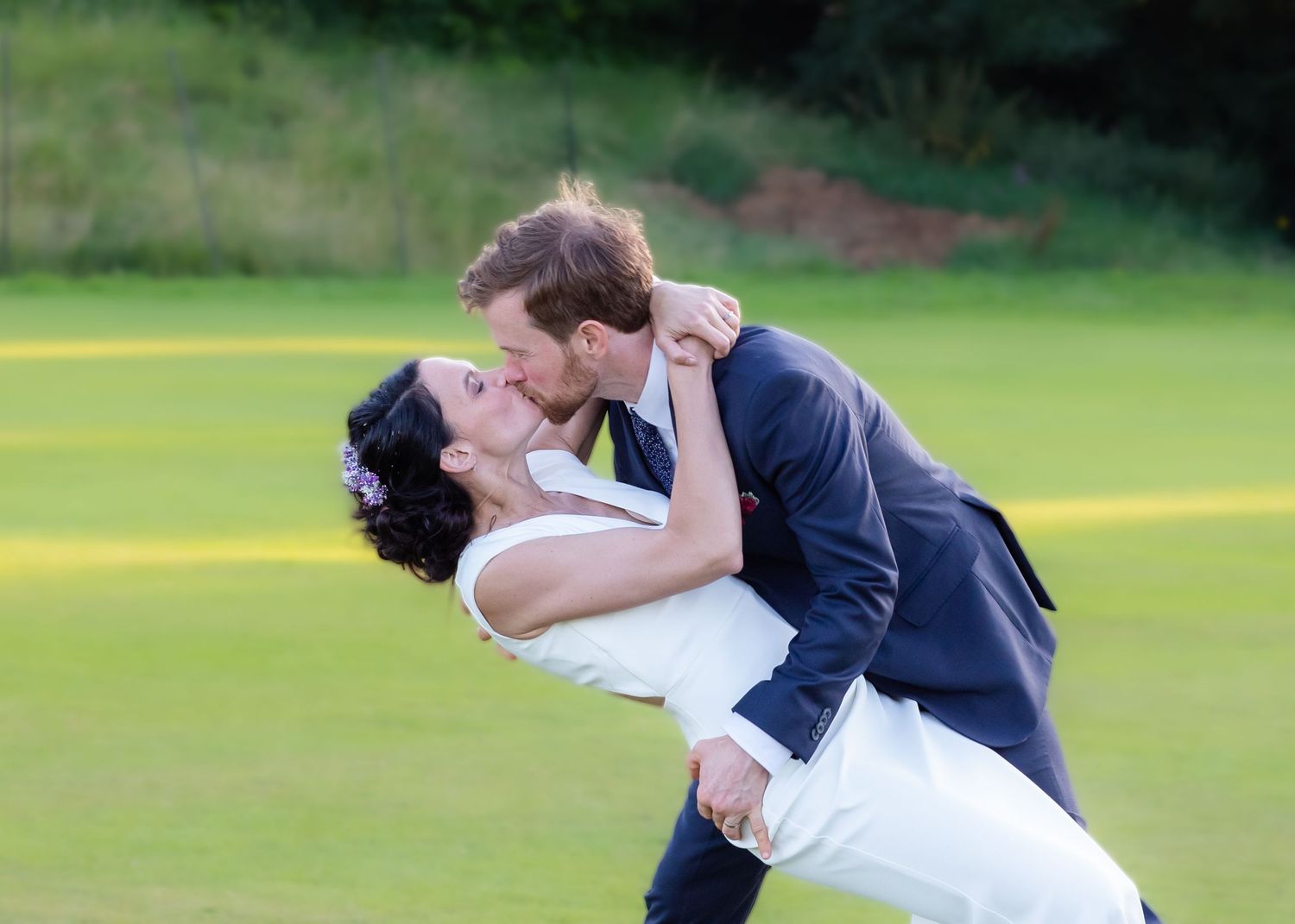 A couple performing a romantic dip pose on a green lawn.