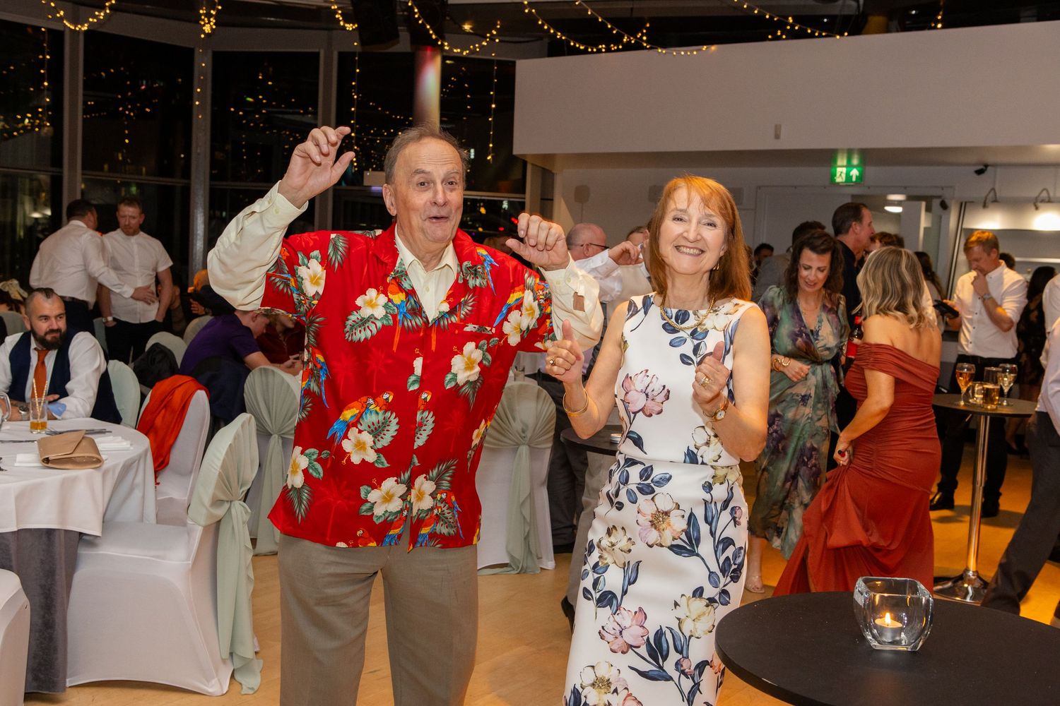People dancing and celebrating at what appears to be a wedding reception or party in an indoor venue.