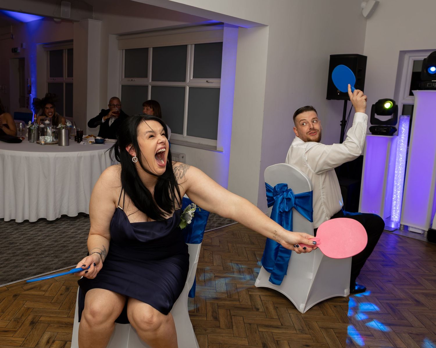Two guests play a fun paddle game at a wedding reception in a decorated banquet hall.