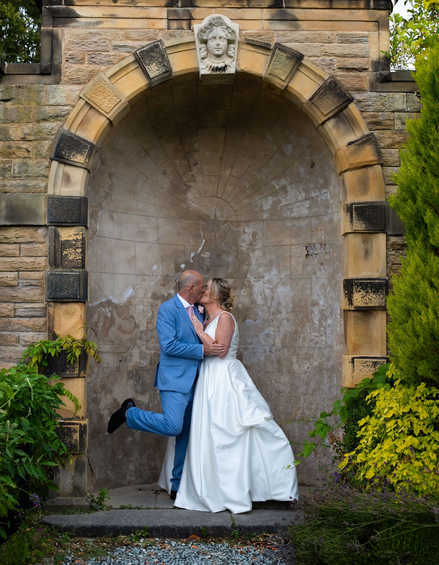 A couple sharing a romantic moment under a stone archway with climbing vines.