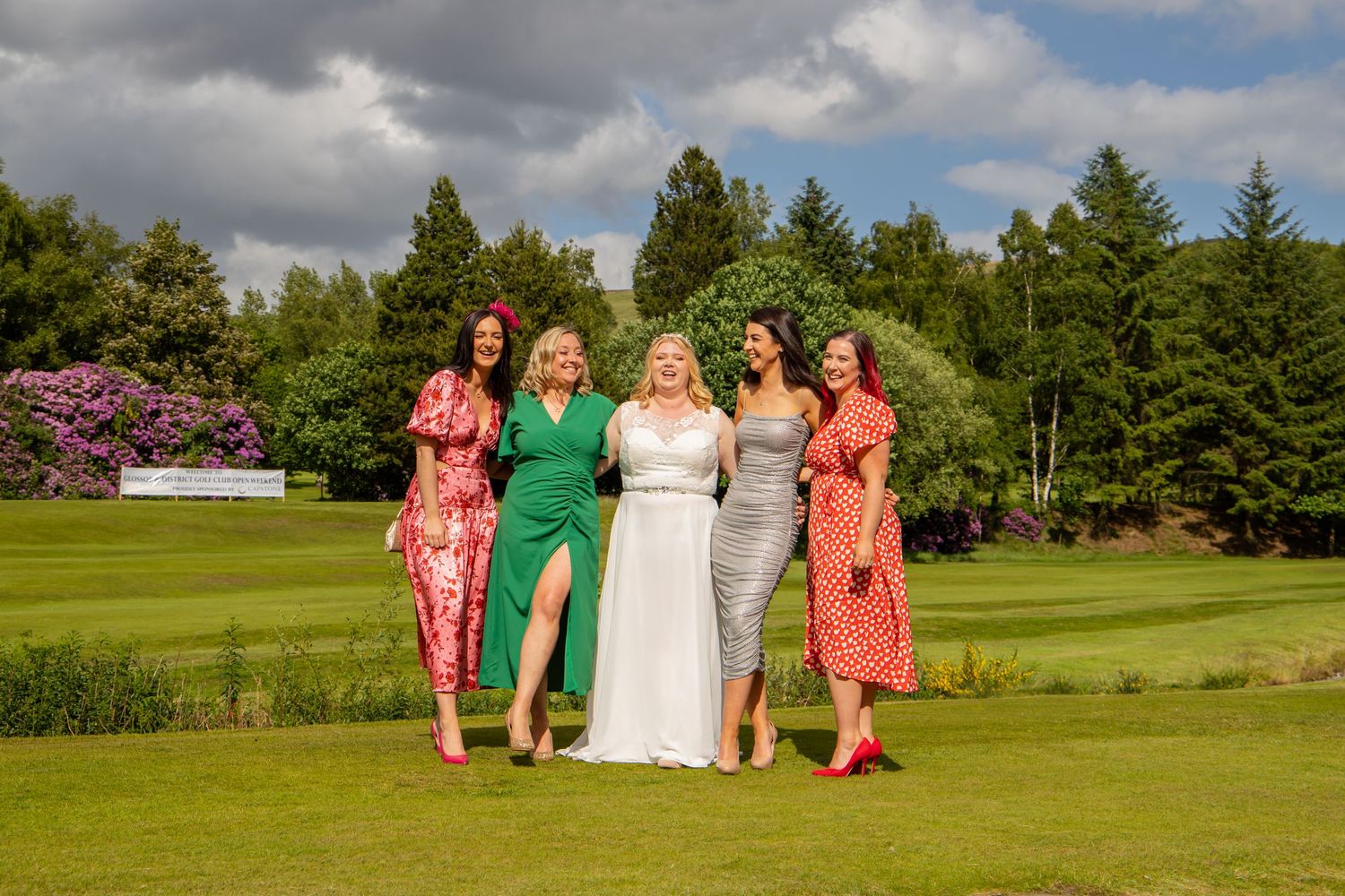 Wedding party poses on golf course with colorful floral backdrop.
