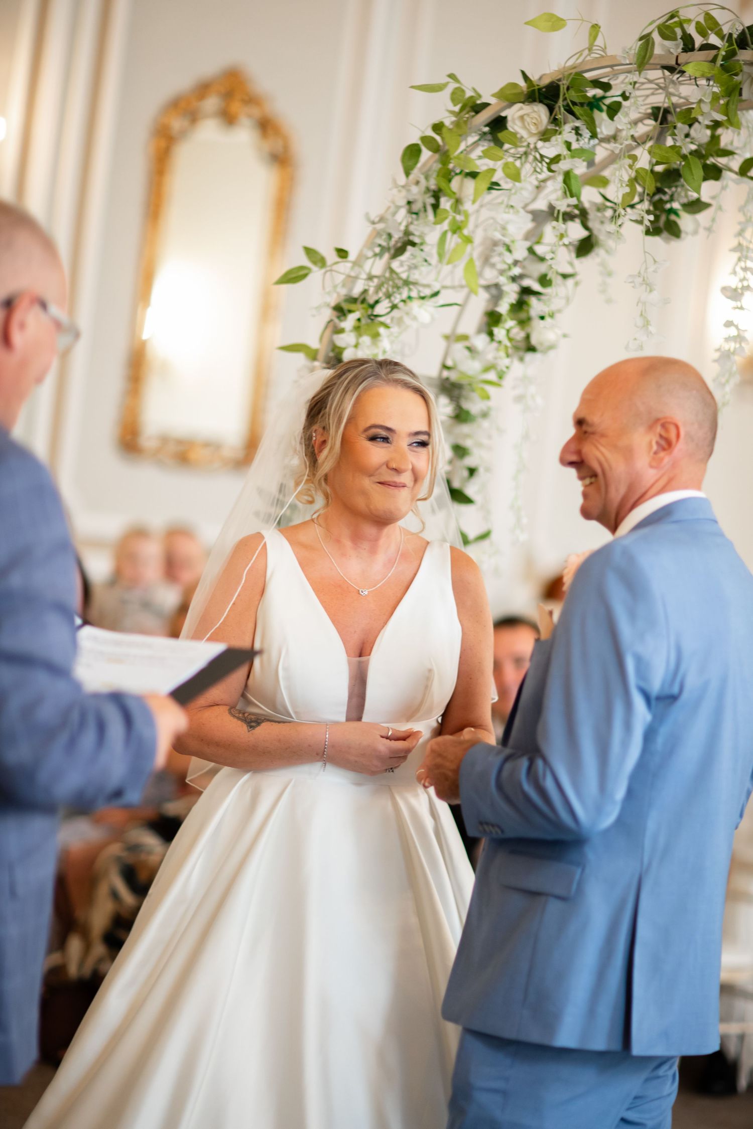 Couple sharing their first dance in an elegant ballroom with floral arrangements overhead.
