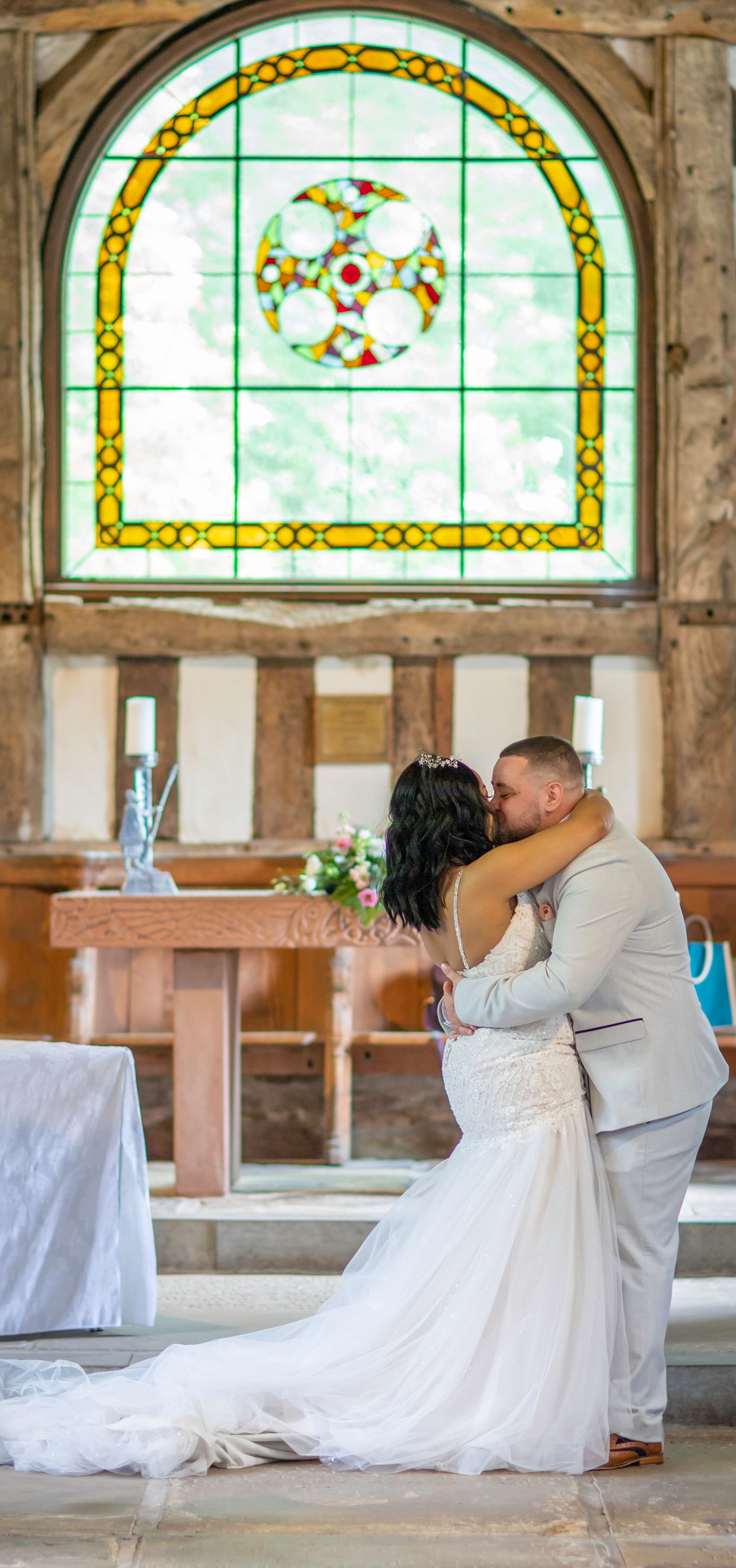Wedding couple dances before stained glass windows in rustic timber-framed venue.