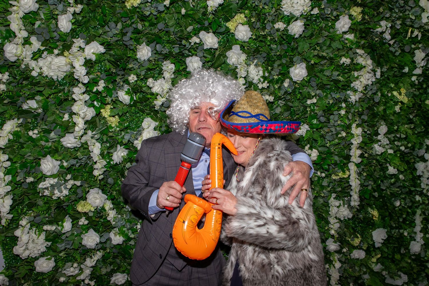 A person in a gray jacket picks white flowers from a blooming garden while holding an orange basket.