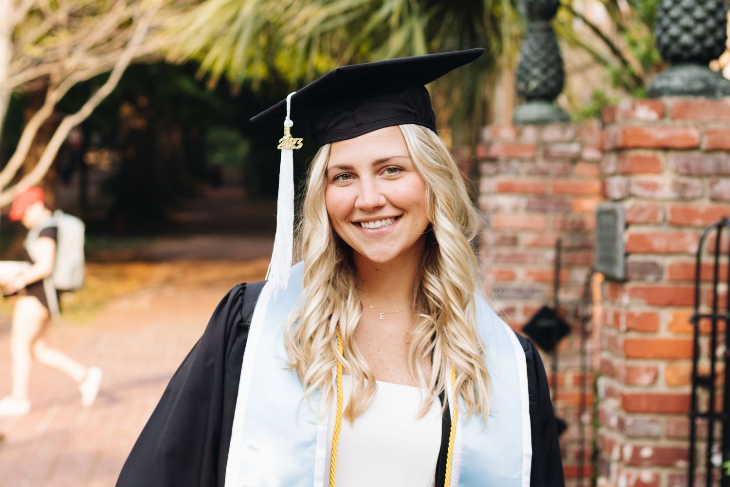 Graduate in cap and gown smiling in front of brick wall during graduation photo session.