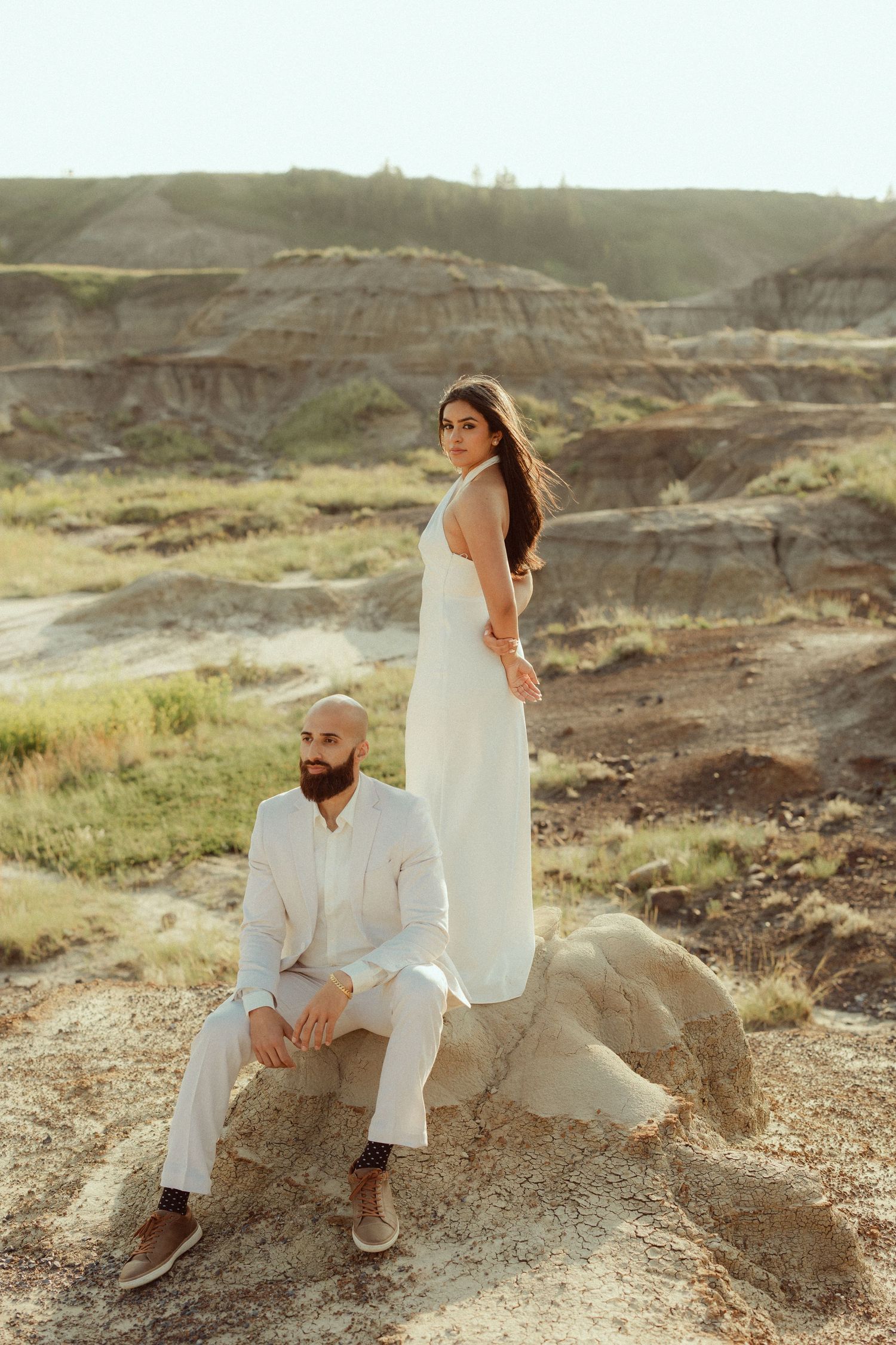 A couple in white outfits poses together on rocky terrain in the Badlands during a sunset photoshoot.